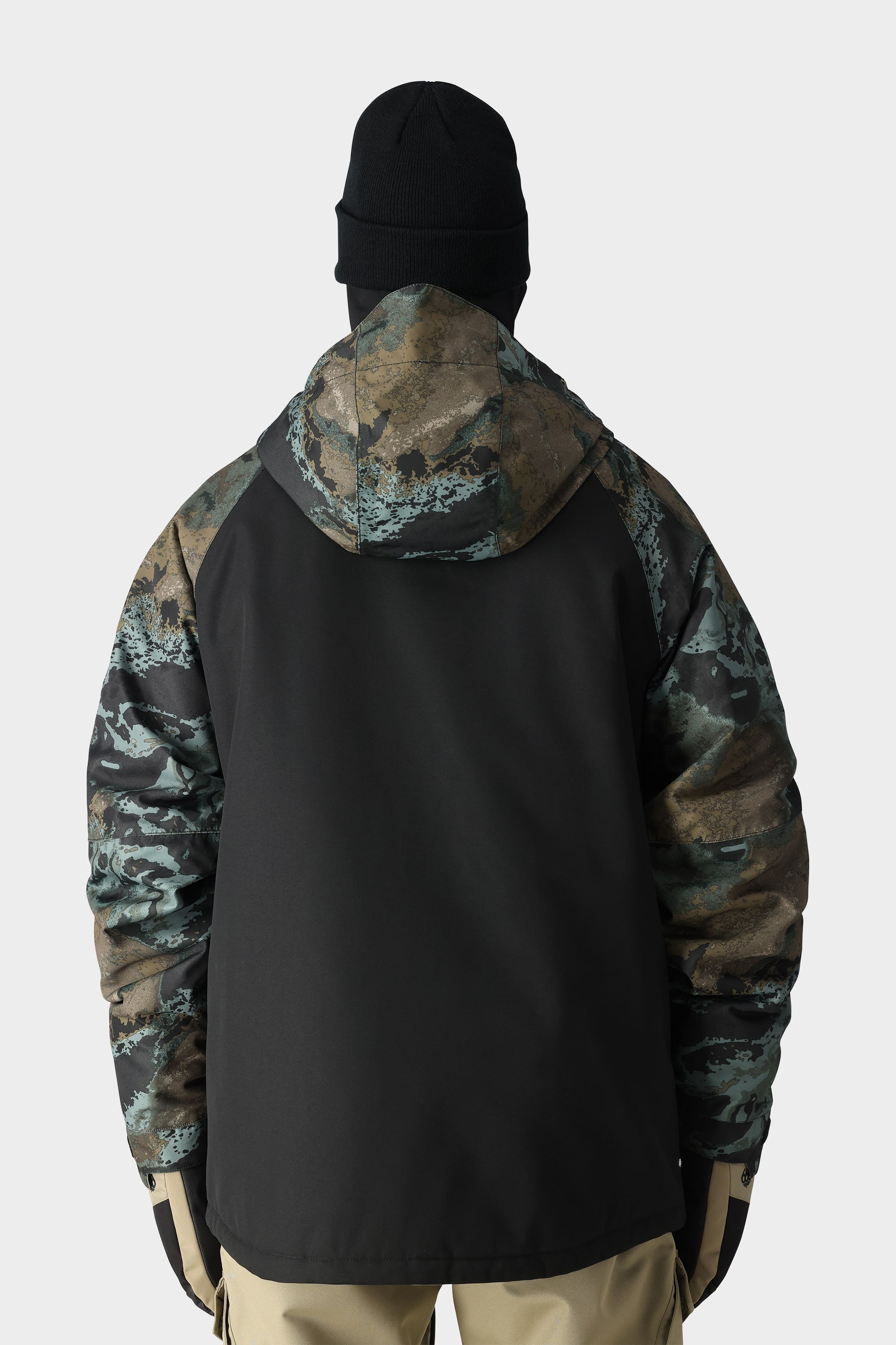 A person in a black beanie wears the 686 Mens Geo Insulated Jacket by 686, shown from behind. The jacket features a black back with camo-patterned sleeves and hood, set against a plain light gray background.