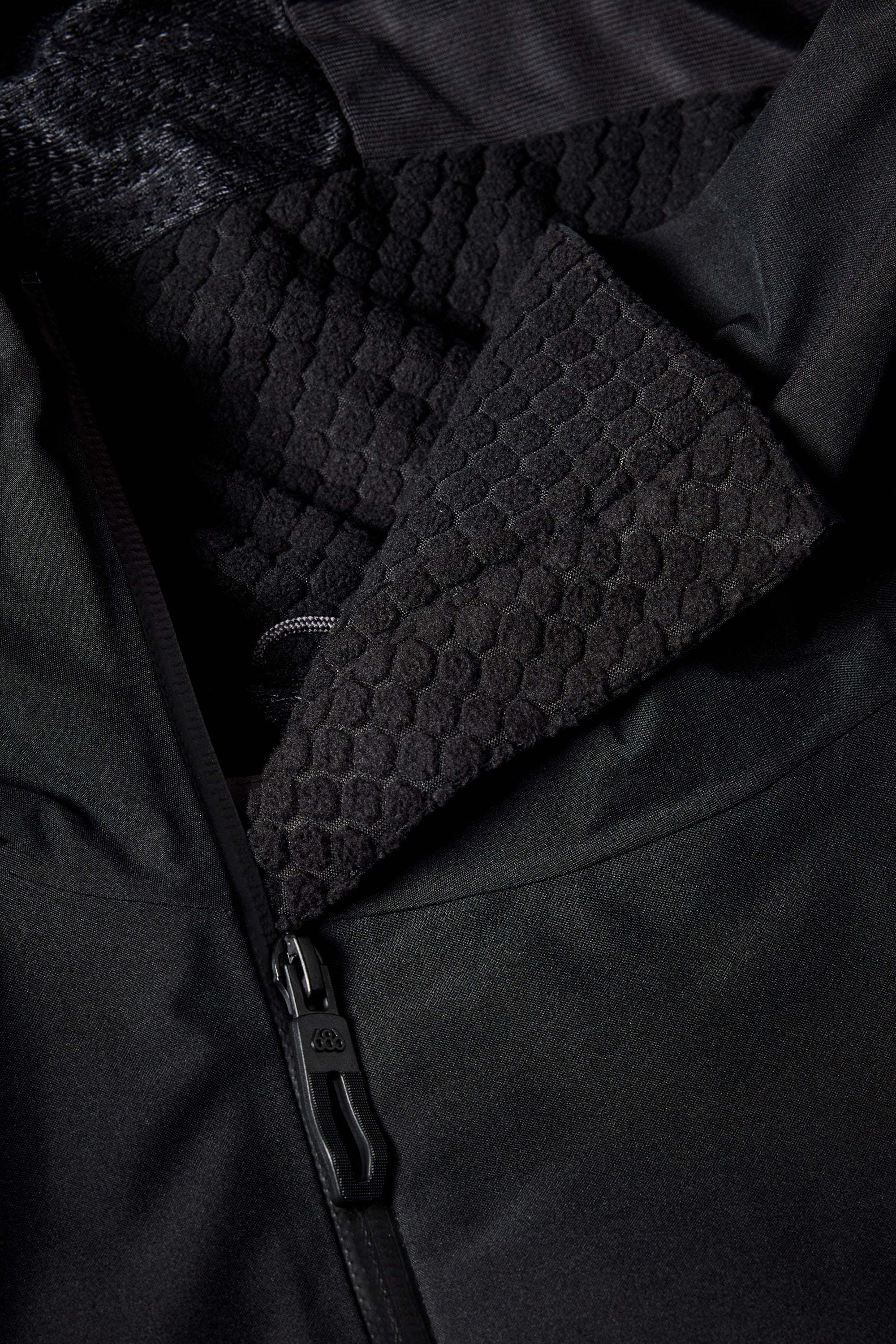 Close-up of the 686 Mens Geo Insulated Jacket by 686, highlighting its matte zipper, hexagonal-patterned textured lining, water-resistant smooth outer fabric, and sleek tech features with the hood also visible.