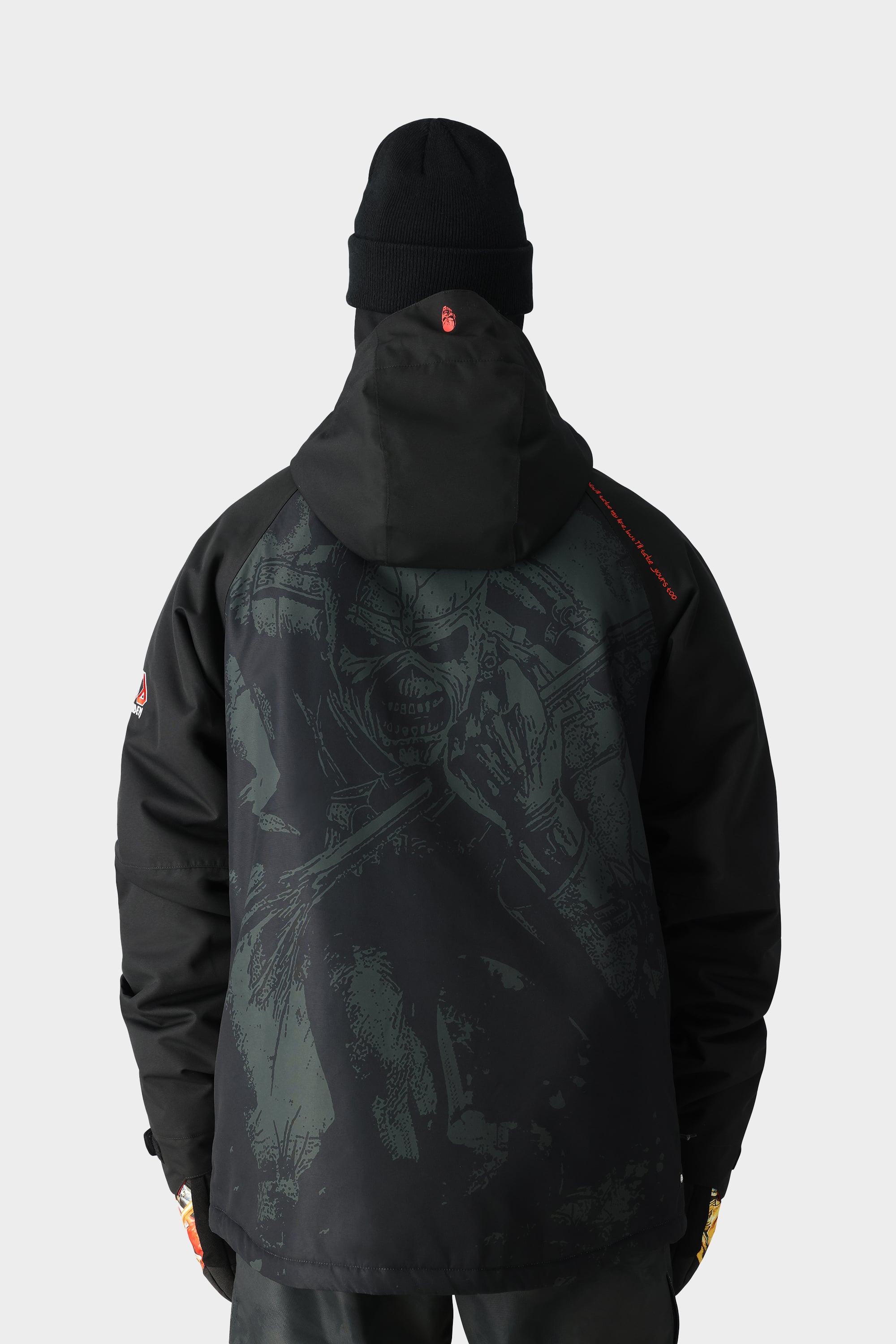 A person wearing a 686 Mens Geo Insulated Jacket and a black beanie, seen from behind, showcases the jacket’s dark, detailed graphic of a menacing face on the back against a plain white background.