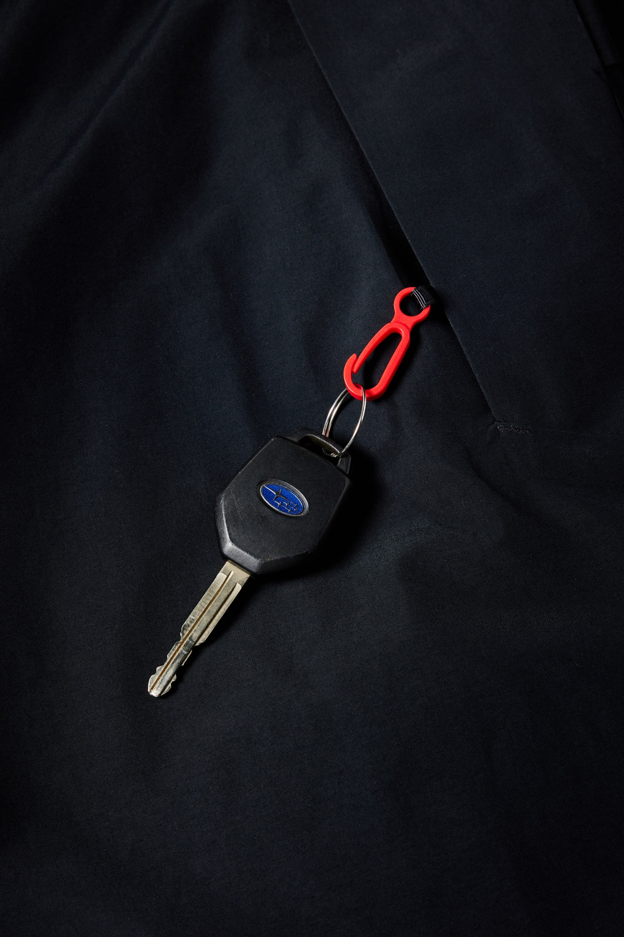 A car key with a black plastic head and a blue oval logo is attached to a small red carabiner clip, resting against the 686 Mens Geo Insulated Jacket by 686.