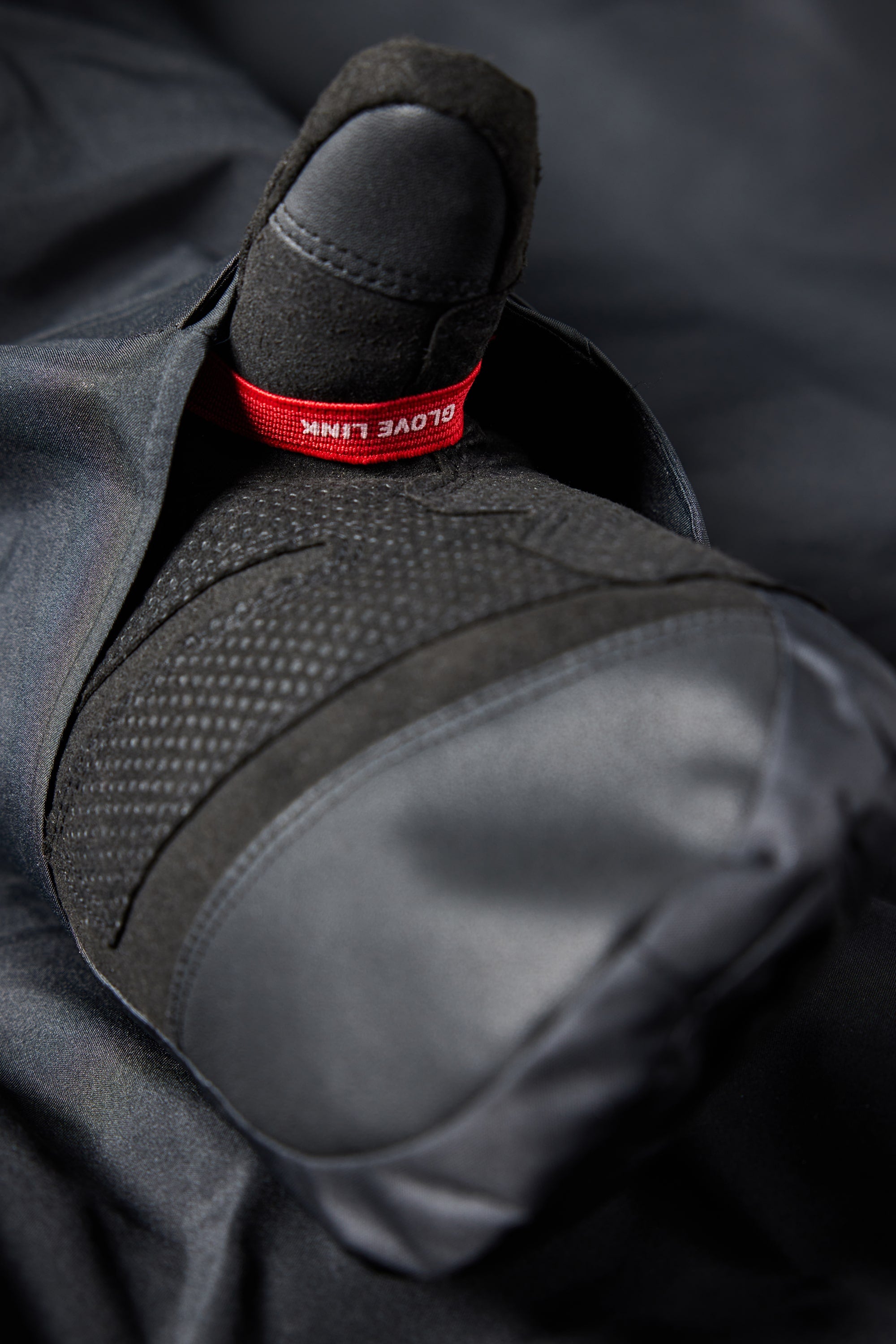 A close-up of a gloved hand with a red tag labeled 686 Mens Geo Insulated Jacket by 686, highlighting its innovative tech features against a dark background.