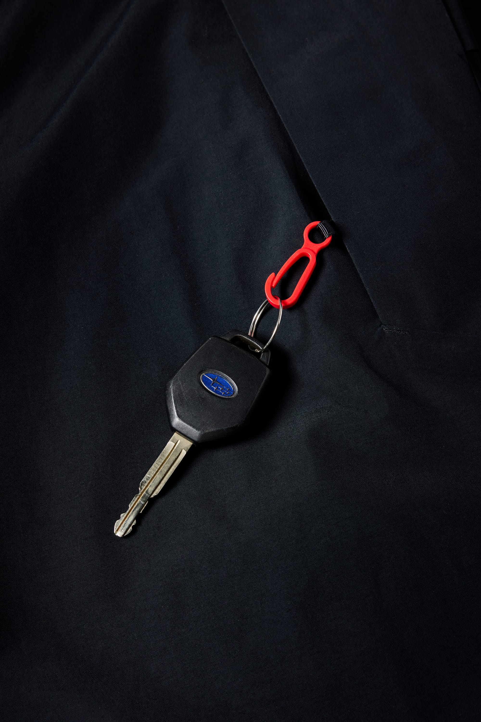 A car key with a blue logo on a red keychain clip sits atop the dark, durable fabric of the 686 Mens GORE-TEX Core Shell Pant by 686.