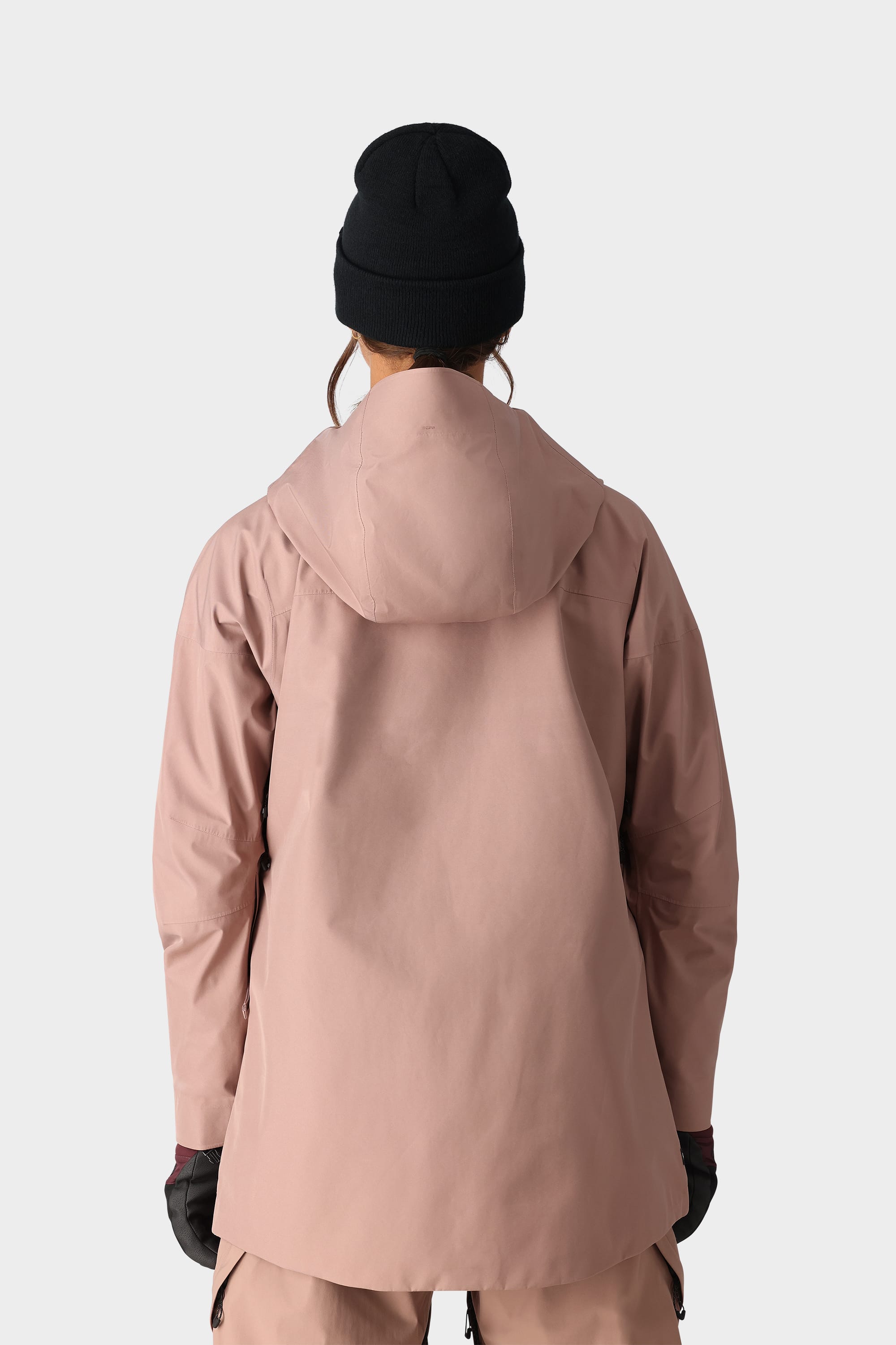 Someone wearing the 686 Womens GORE-TEX Skyline Shell Jacket in pink, matching pants, black gloves, and a black beanie stands with their back to the camera against a plain light background.