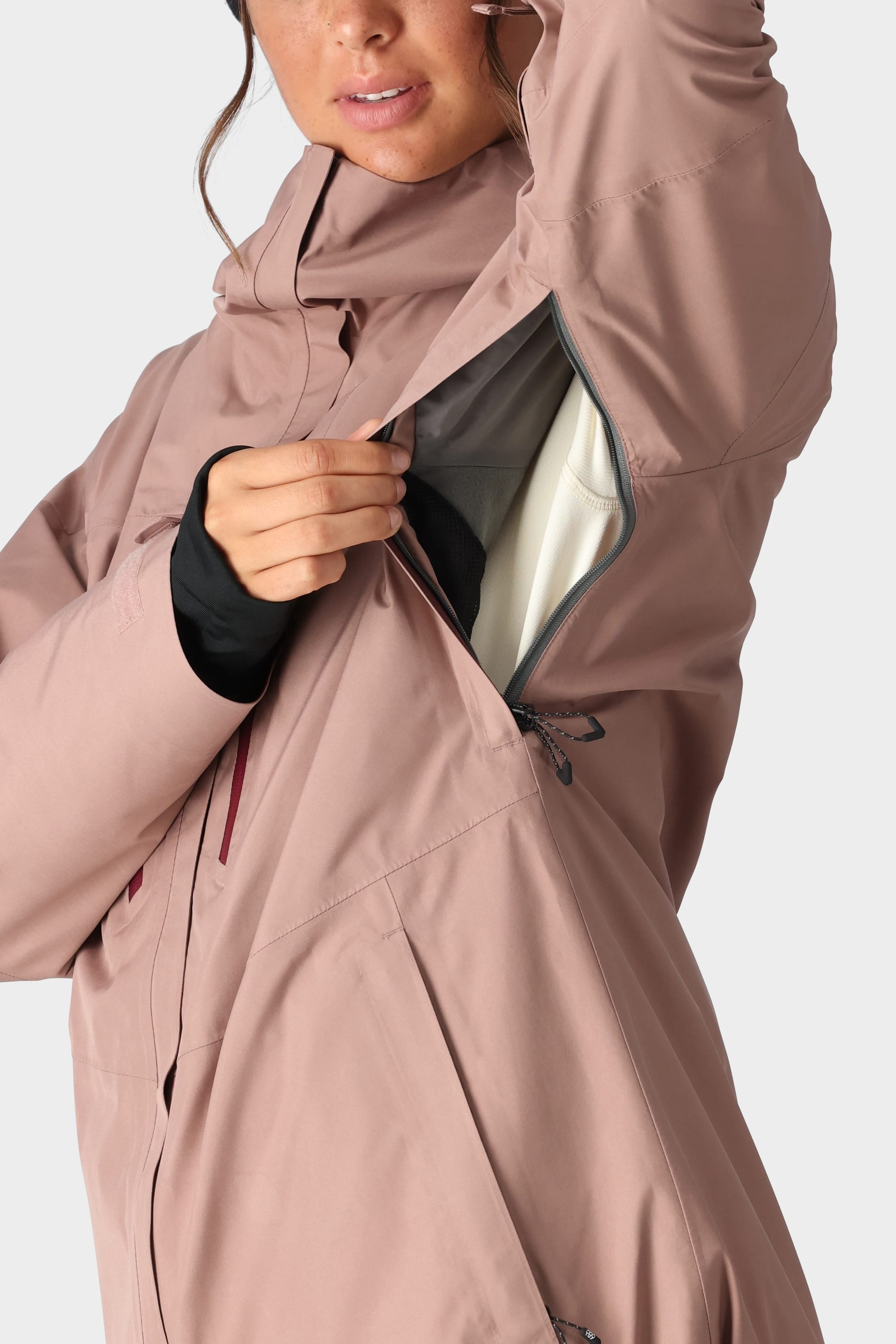 A woman in the 686 Womens GORE-TEX Skyline Shell Jacket by 686 partially unzips the underarm vent, revealing its light-colored, body-mapped lining.