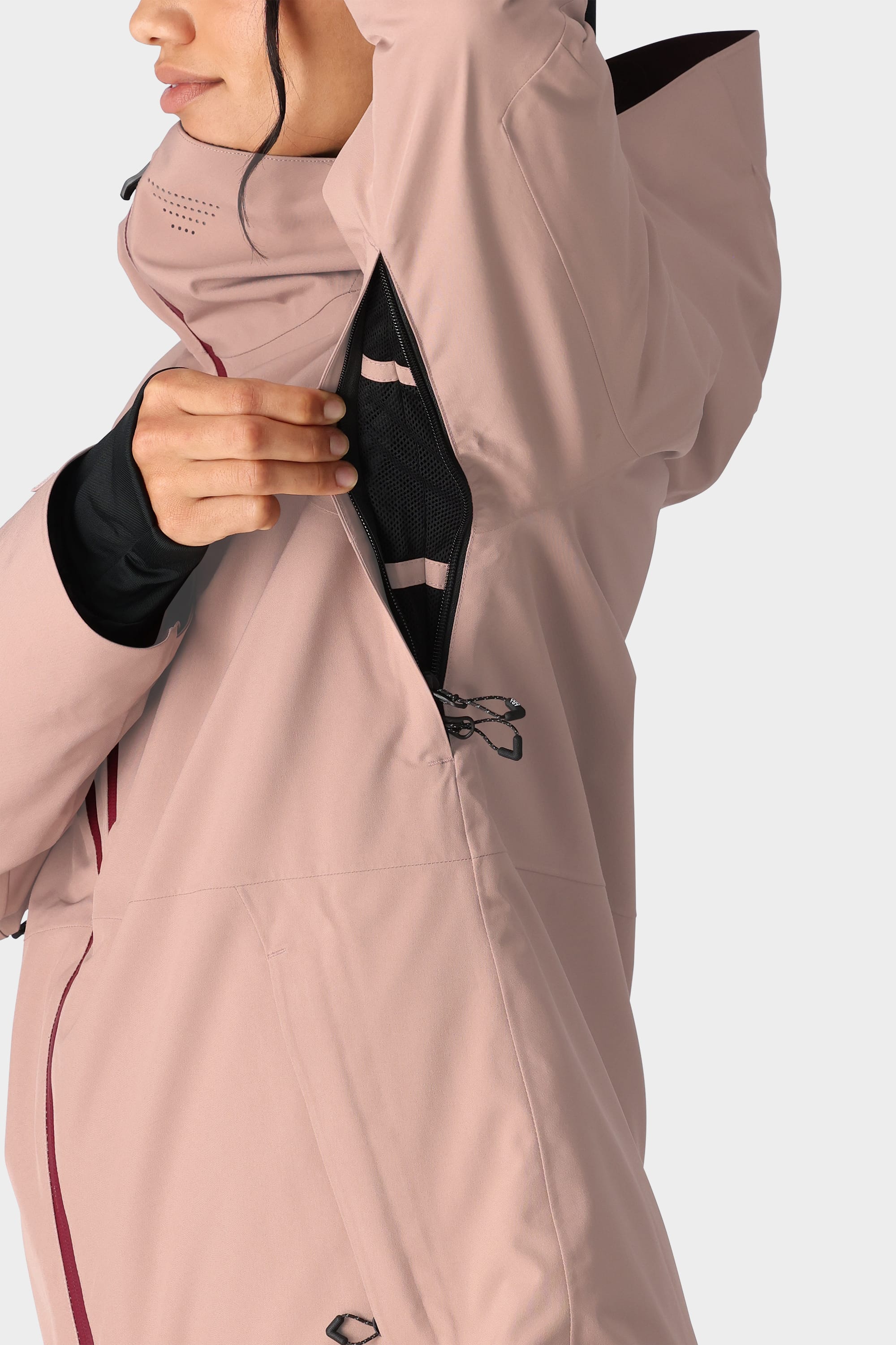 A person partially unzips the underarm vent of a 686 Womens Hydra Insulated Jacket in light pink, revealing black mesh lining inside; only the lower half of their face and body are visible.