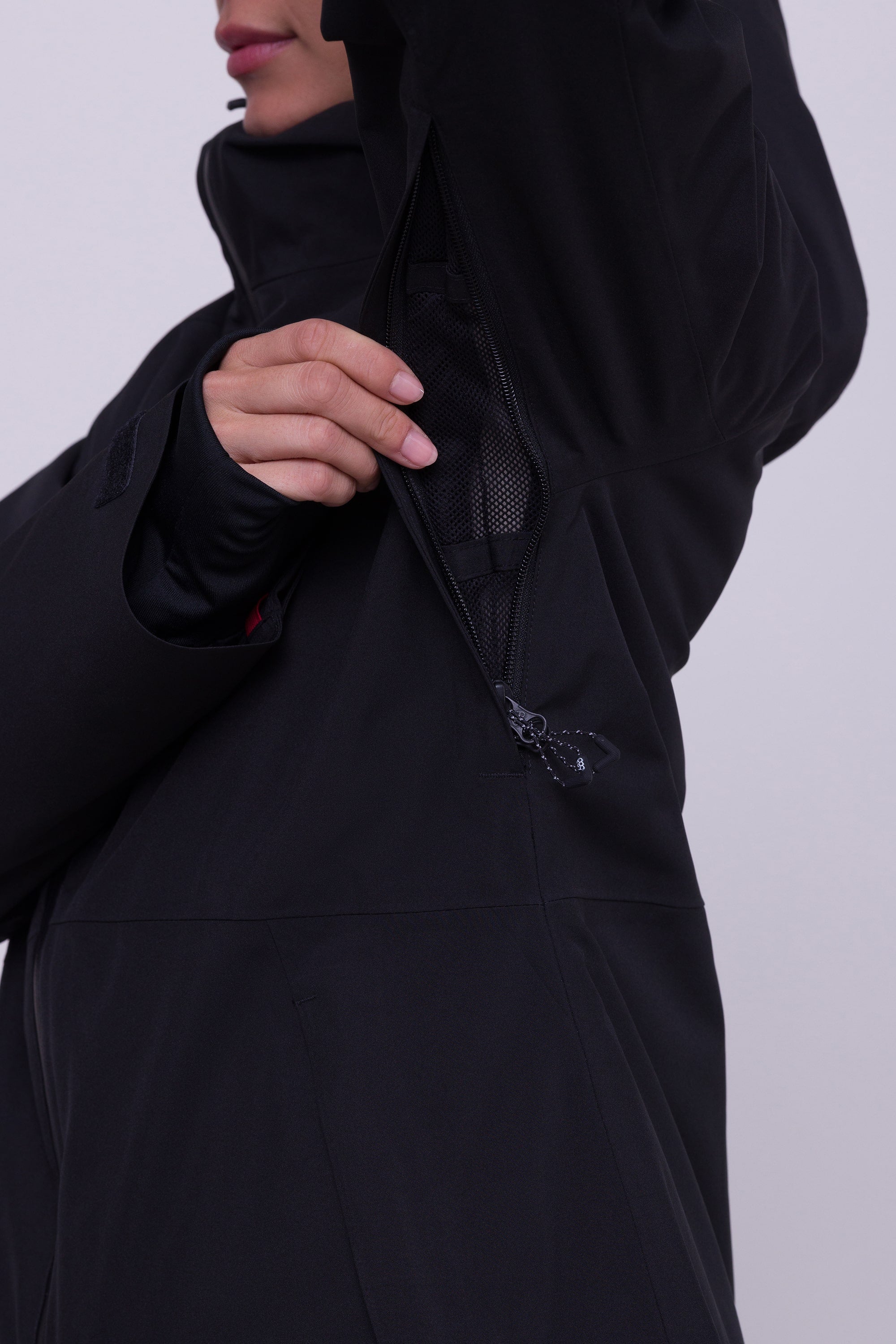A woman in the 686 Womens Hydra Insulated Jacket unzips an underarm vent to show the mesh lining. The photo is cropped to display only her lower face and upper body.