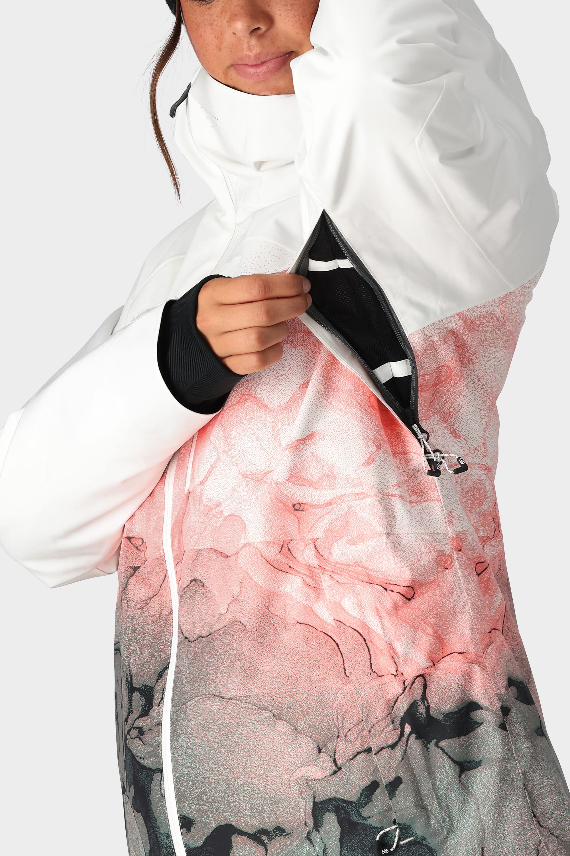 A woman in the 686 Womens Hydra Insulated Jacket unzips a black-zippered underarm vent, showing mesh lining and light insulation. Only her lower face and upper body are visible.