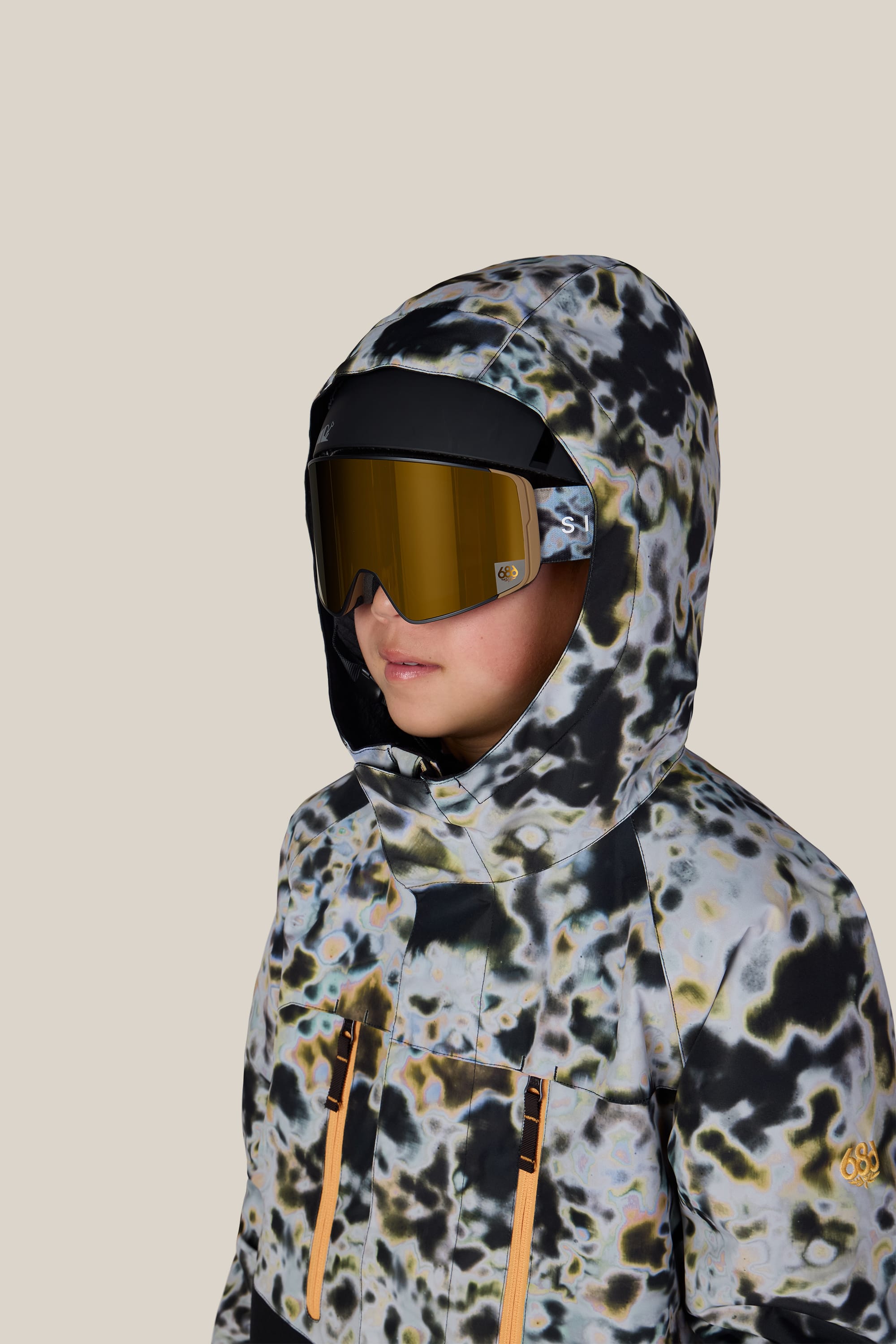 A person wearing the 686 Boys’ Geo™ Insulated Jacket by 686, styled with large yellow ski goggles and facing slightly to the left, set against a plain beige background.