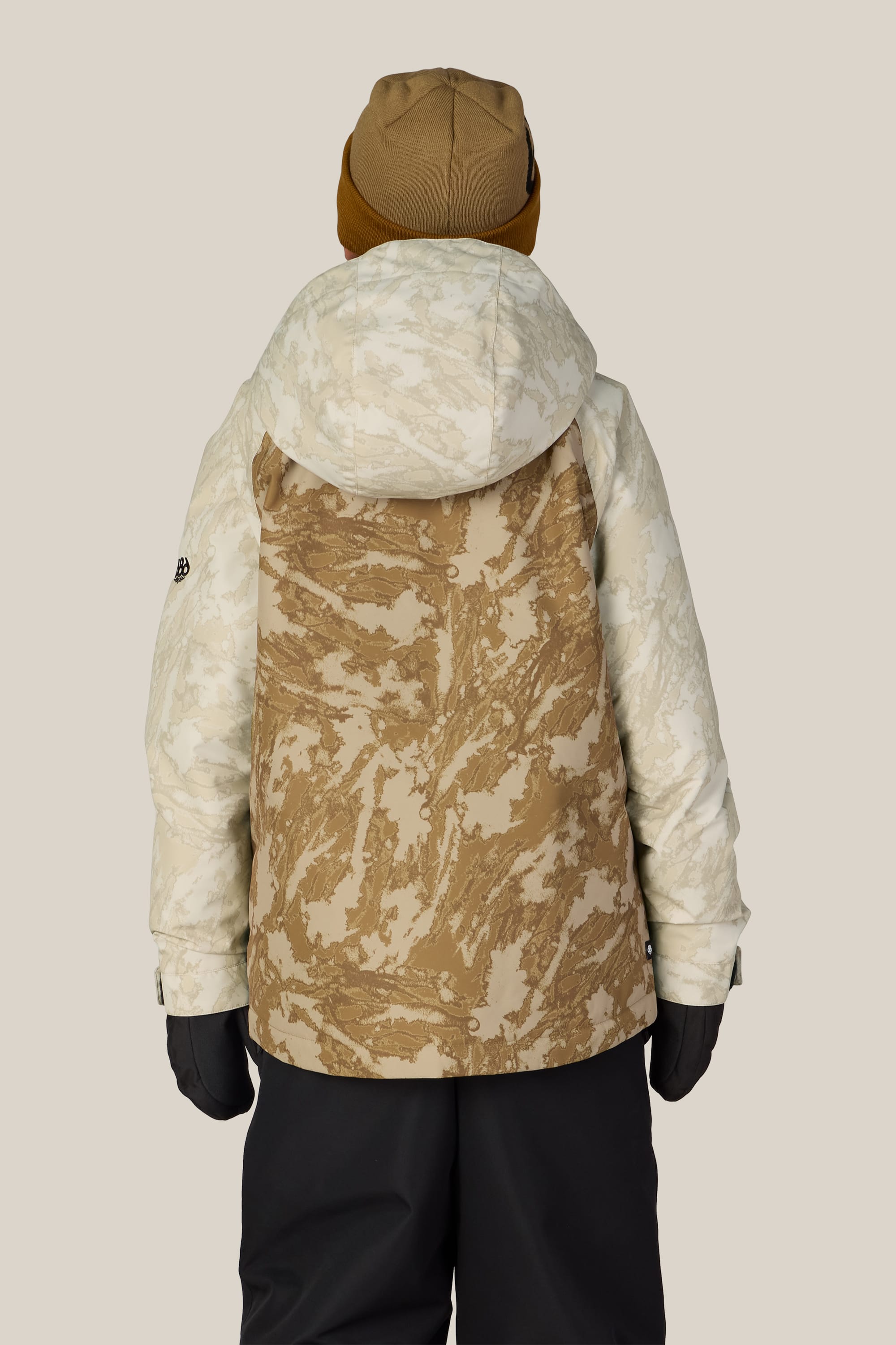 A person wearing the 686 Boys’ Geo™ Insulated Jacket by 686 stands with their back to the camera against a plain background, paired with a brown beanie, black gloves, and black pants.