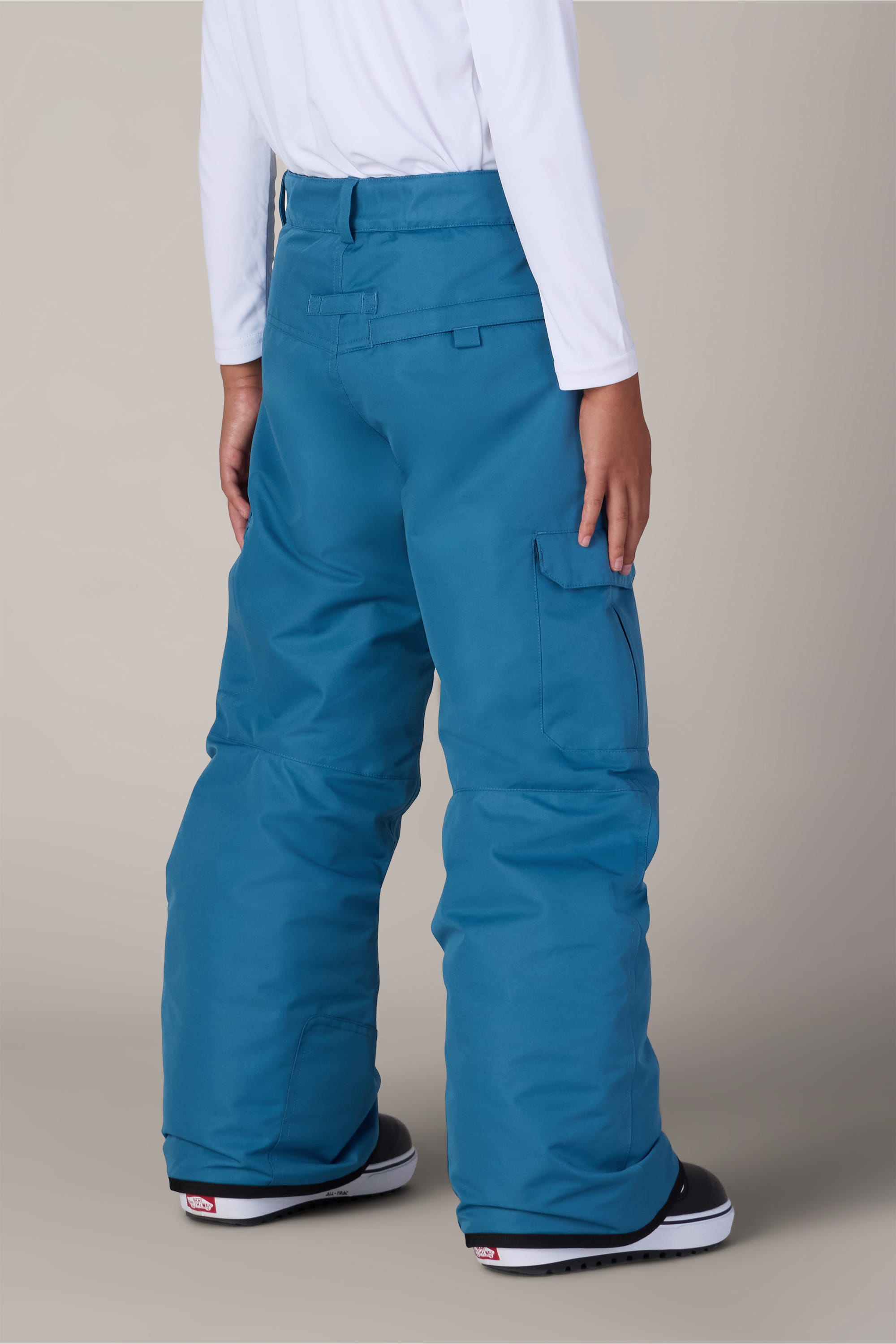 A person is shown from the back against a plain background, wearing the 686 Boys Infinity™ Cargo Insulated Pant in a loose-fitting blue style, paired with a white long-sleeve shirt and black-and-white snow boots.