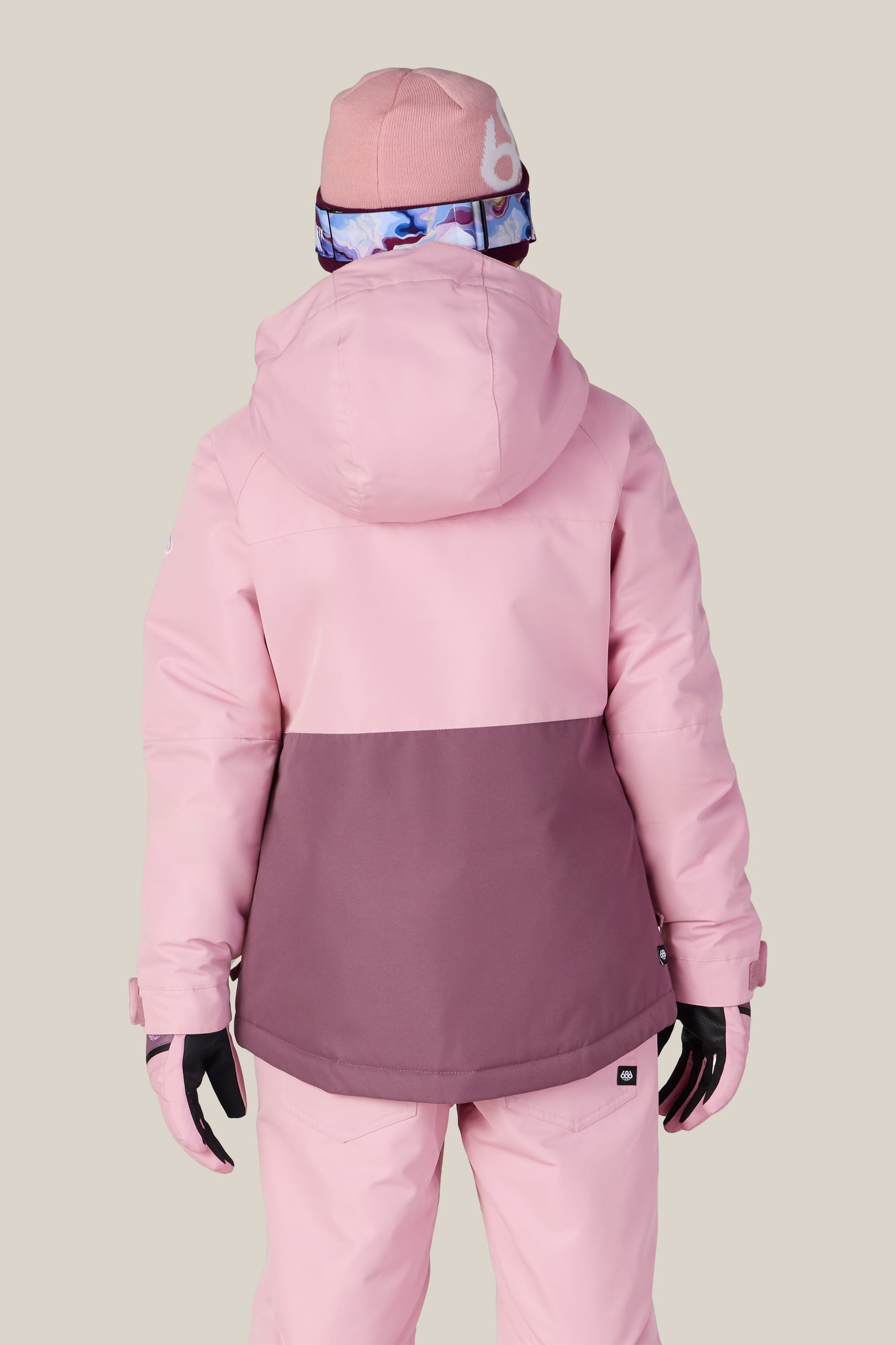 A person is facing away from the camera against a plain light background, wearing the 686 Girls’ Athena™ Insulated Jacket by 686 in two-tone pink and mauve, along with pink snow pants, a pink beanie, gloves, and goggles.