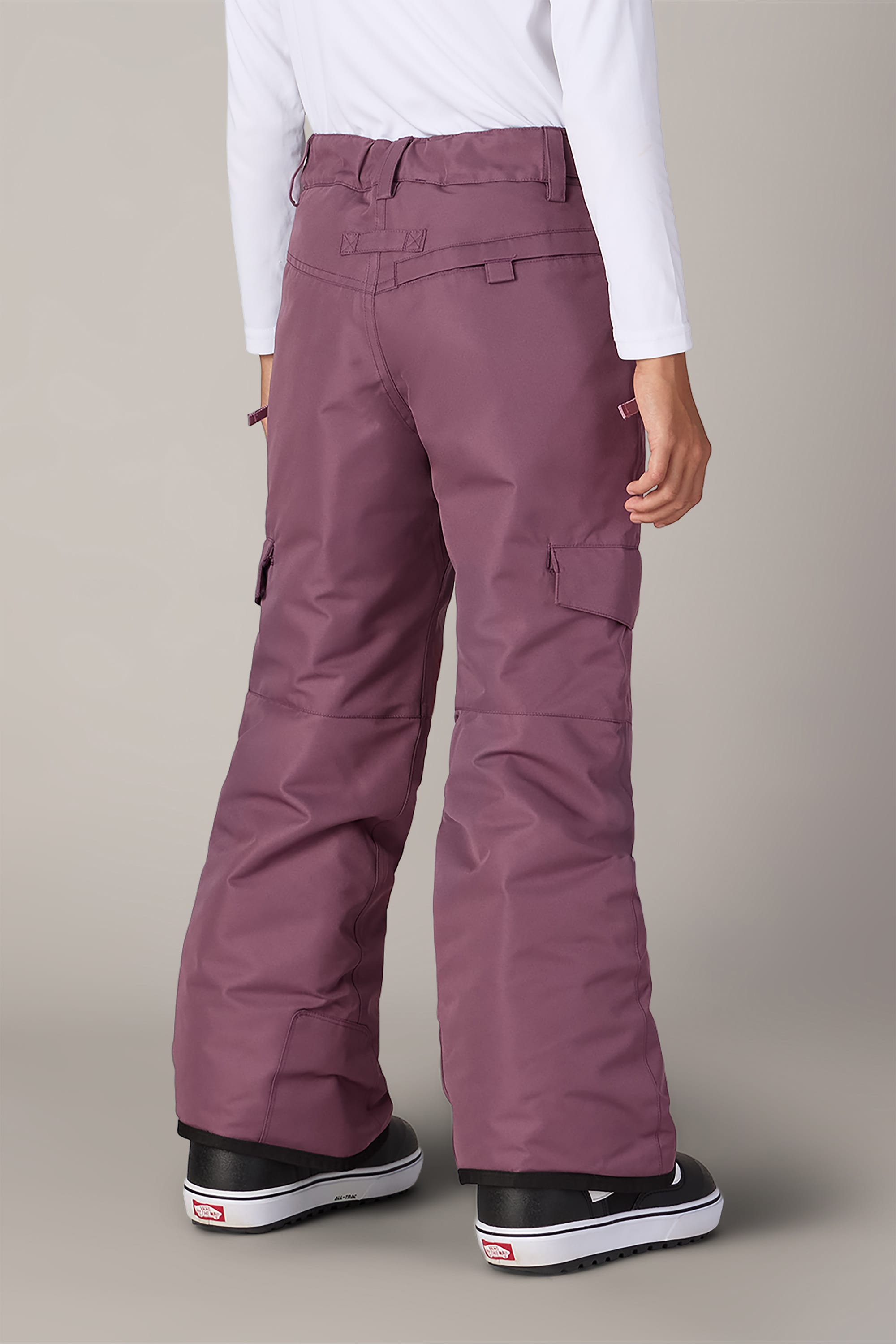 A person is standing facing away from the camera against a plain background, wearing 686 Girls’ Lola Insulated Pants in mauve with light insulation, a white long-sleeve shirt, and black Vans sneakers.