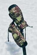 A pair of 686 Lander Mitts with light insulation are displayed on crossed ski poles against a snowy backdrop.