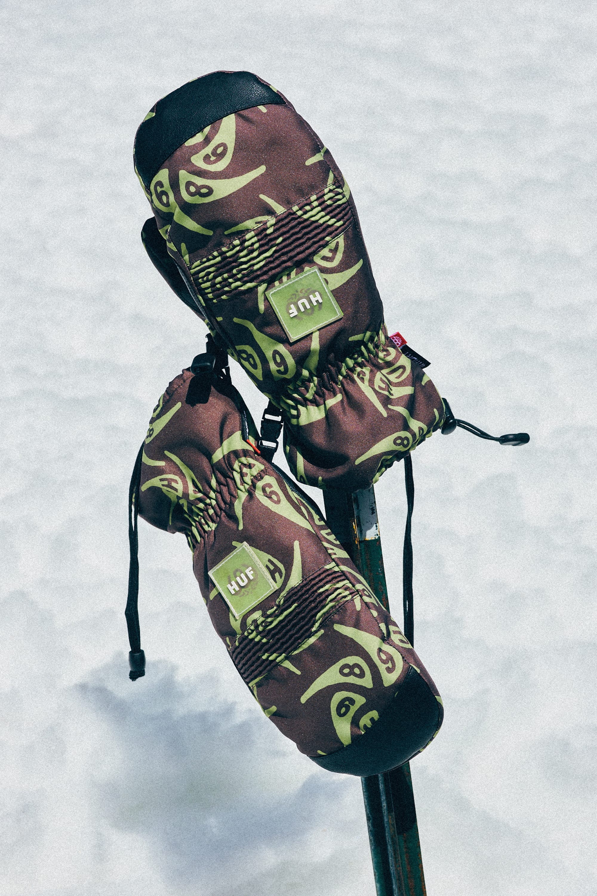 A pair of 686 Lander Mitts with light insulation are displayed on crossed ski poles against a snowy backdrop.