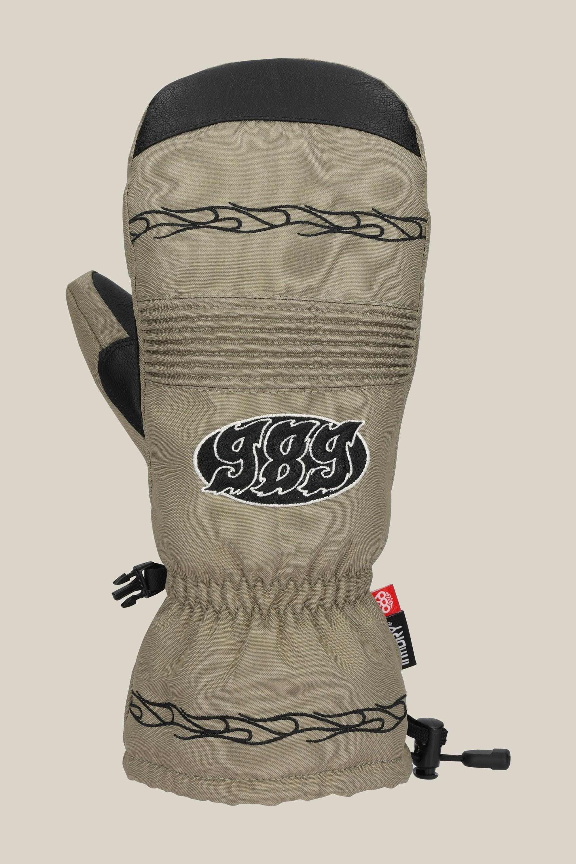 The 686 Lander Mitt by 686 features a beige body, black decorative stitching, black thumb and top patch, embroidered 989 logo on the front, light insulation for warmth, adjustable wrist cord, and a small red side tag.