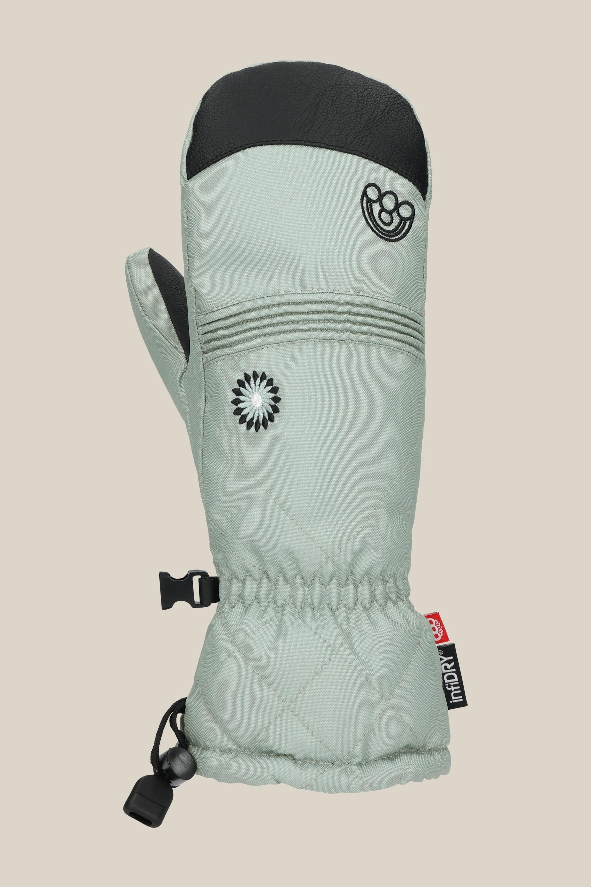The 686 Womens Jubilee Mitt by 686 is a light gray quilted winter mitten with a black thumb, knuckle patch, elastic wrist, daisy and smiley embroidery, adjustable drawcord, and logo tag, offering light insulation for cozy comfort.