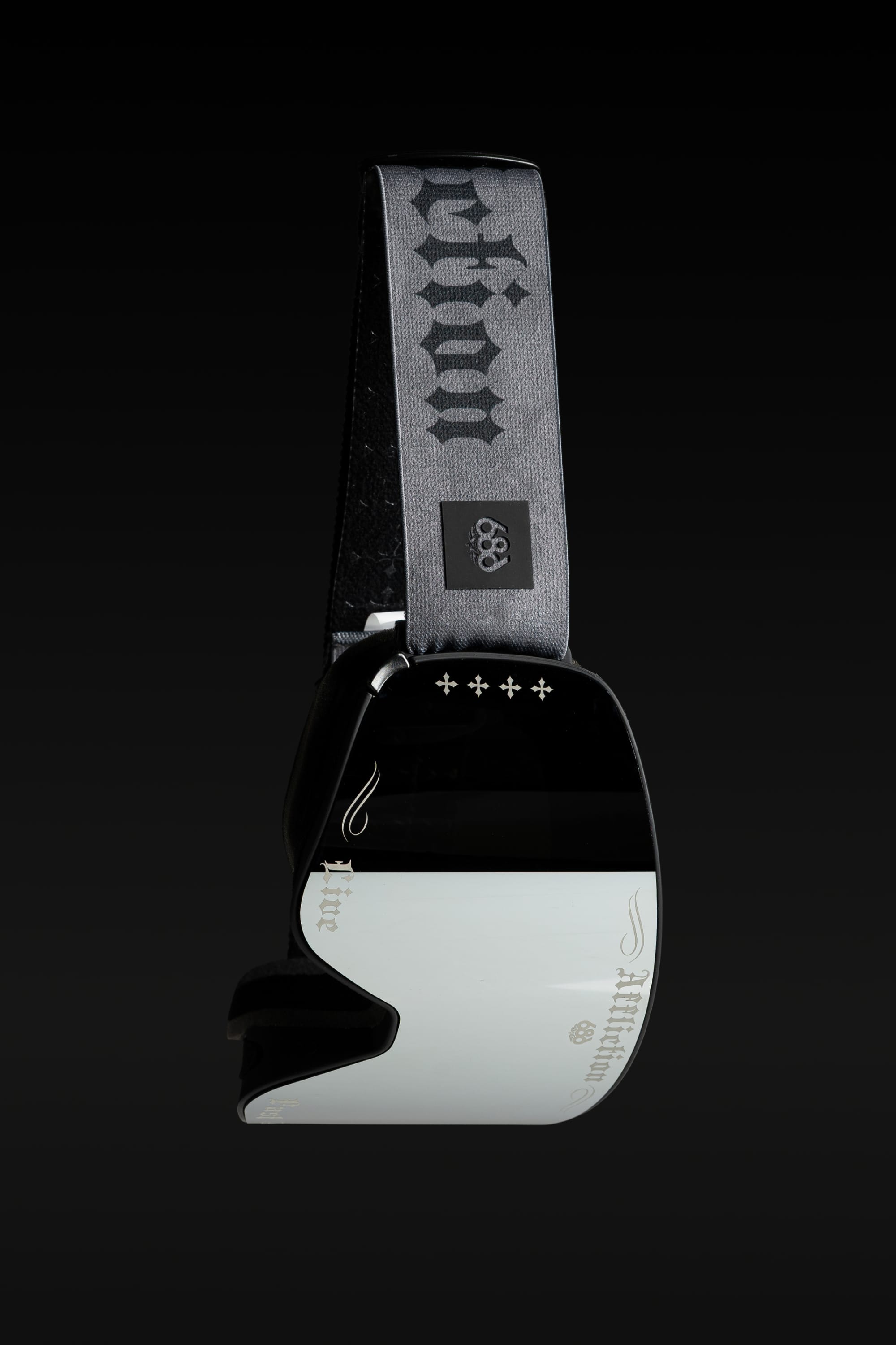 The 686 SMARTY® Magnetic Goggle by 686 features a sleek black and white design, a reflective lens, and a gray strap with stylized text and Olympic rings, set against a dark background.