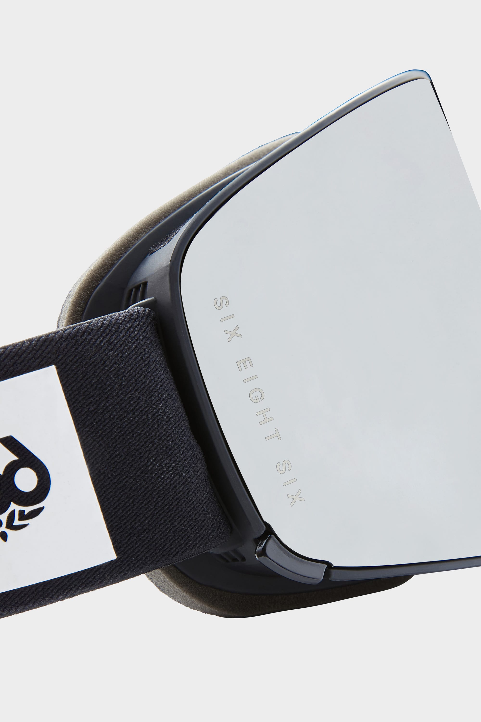 Close-up of the 686 SMARTY Goggle by 686, featuring a minimalist design with SIX EIGHT SIX etched on the reflective lens and a black strap with a white logo patch—engineered for all conditions.