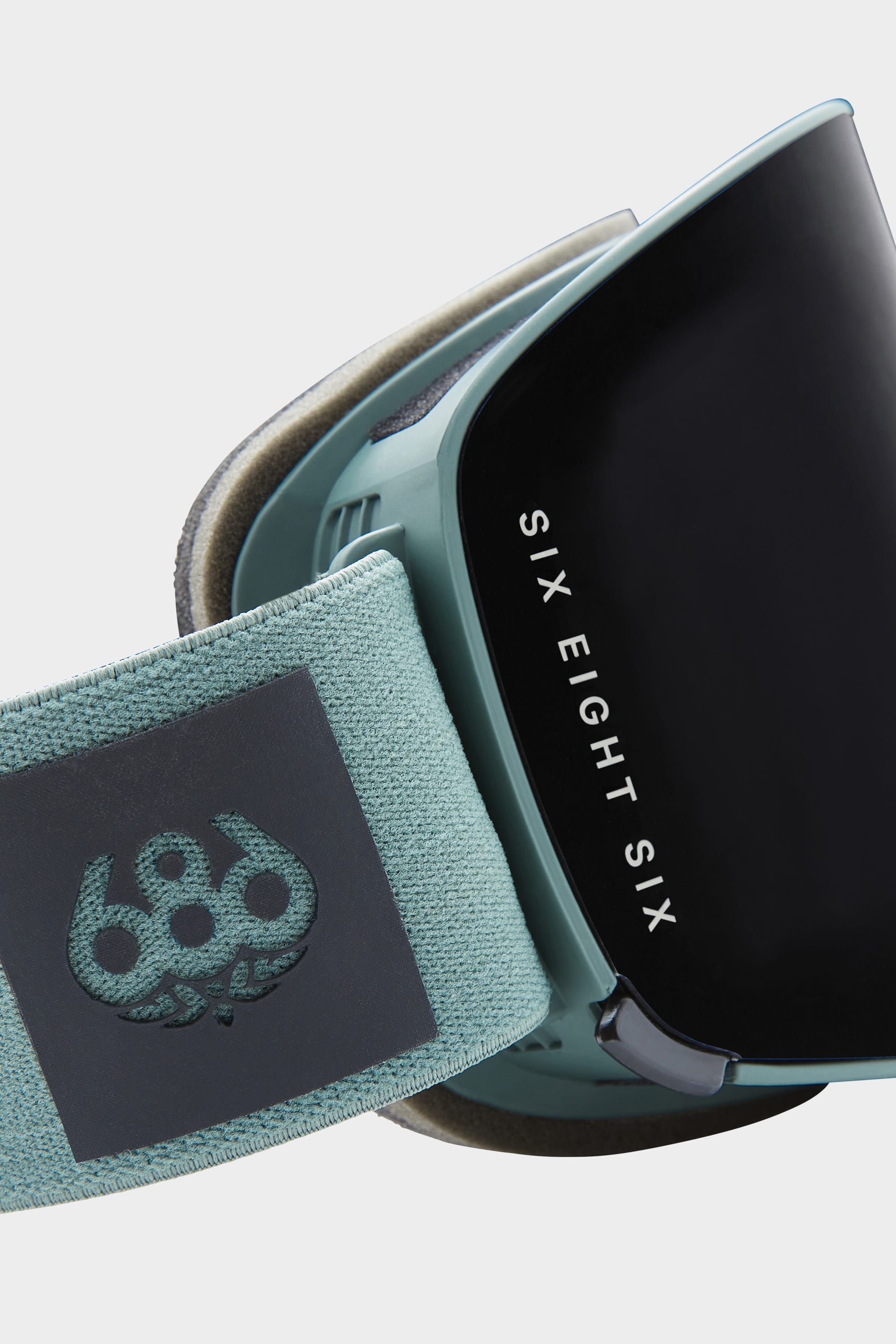 Close-up of the 686 SMARTY Goggle: a teal, minimalist design with a black magnetic lens, 686 logo on the strap, and SIX EIGHT SIX text on the side—perfect for all conditions.
