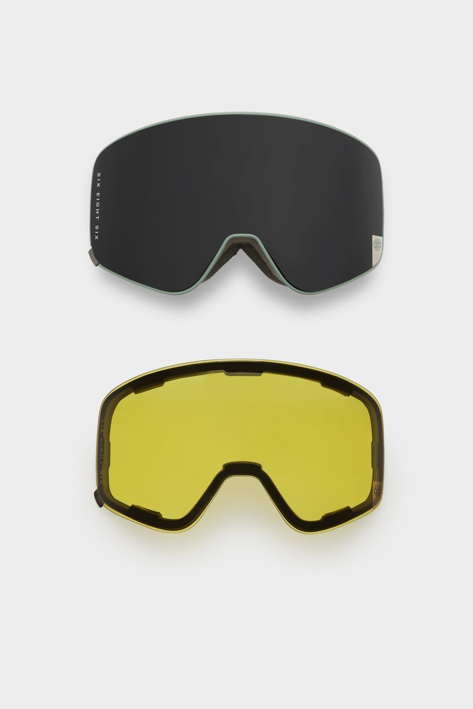 Two interchangeable magnetic lenses for the 686 SMARTY Goggle by 686 are shown: one dark, one yellow-tinted. Both feature a curved, frameless design ideal for all conditions. Displayed on a plain white background.