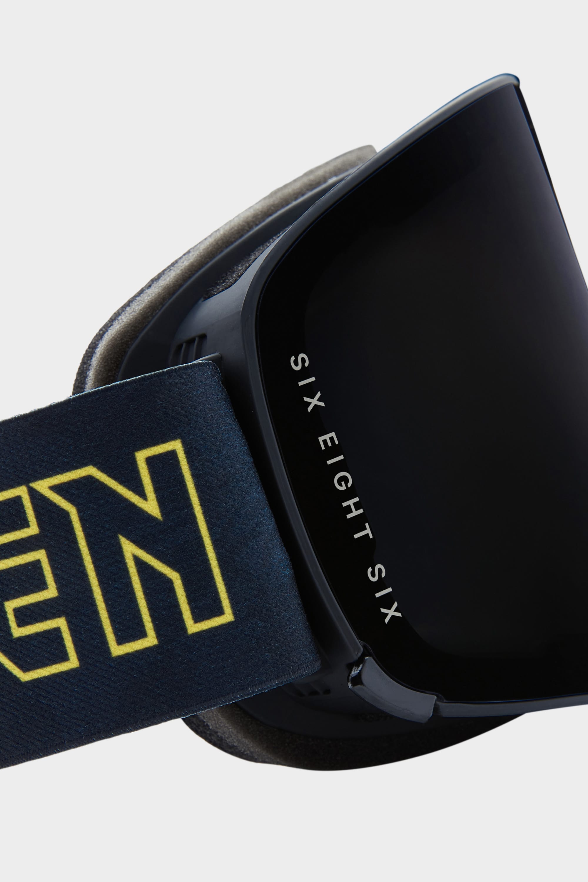 Close-up of 686 SMARTY Goggle, a black minimalist design with “SIX EIGHT SIX” on the magnetic lens, suited for all conditions, and a dark strap with bold yellow lettering.