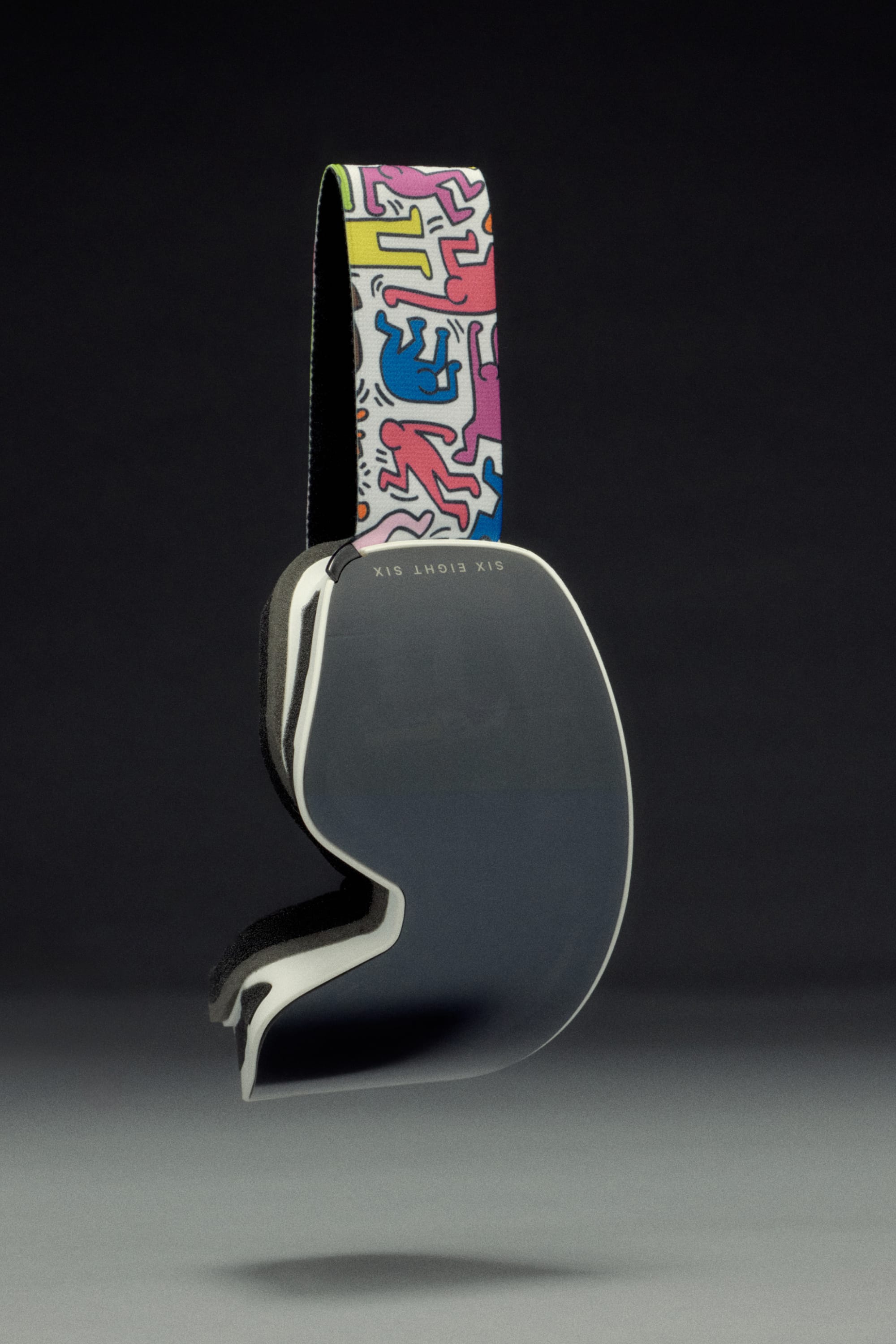 The 686 SMARTY Goggle by 686 features magnetic lenses, a dark reflective lens, and a vibrant Keith Haring-inspired head strap—designed for all conditions and shown against a dark background.