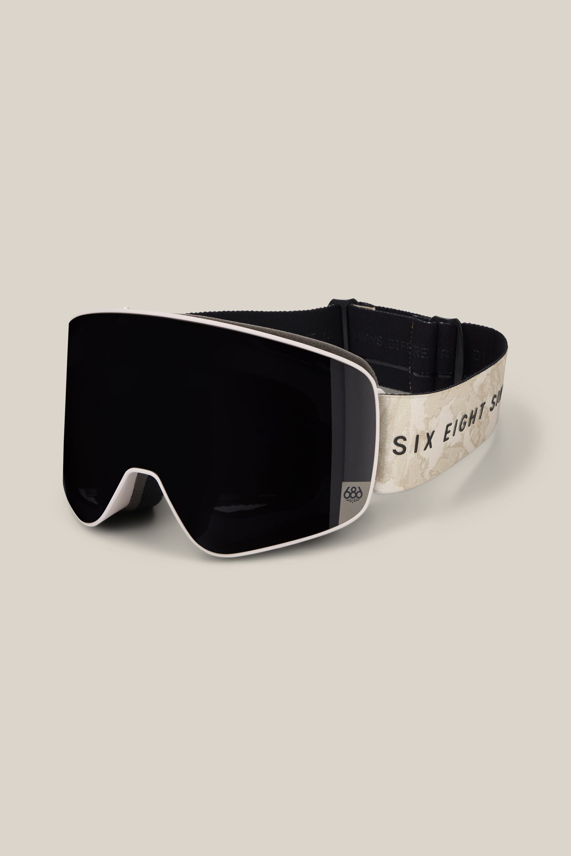 The 686 SMARTY® Magnetic Goggle by 686 features a wide black lens and a cream-colored strap adorned with the text “SIX EIGHT SIX” in black letters. The goggles are shown against a plain beige background.