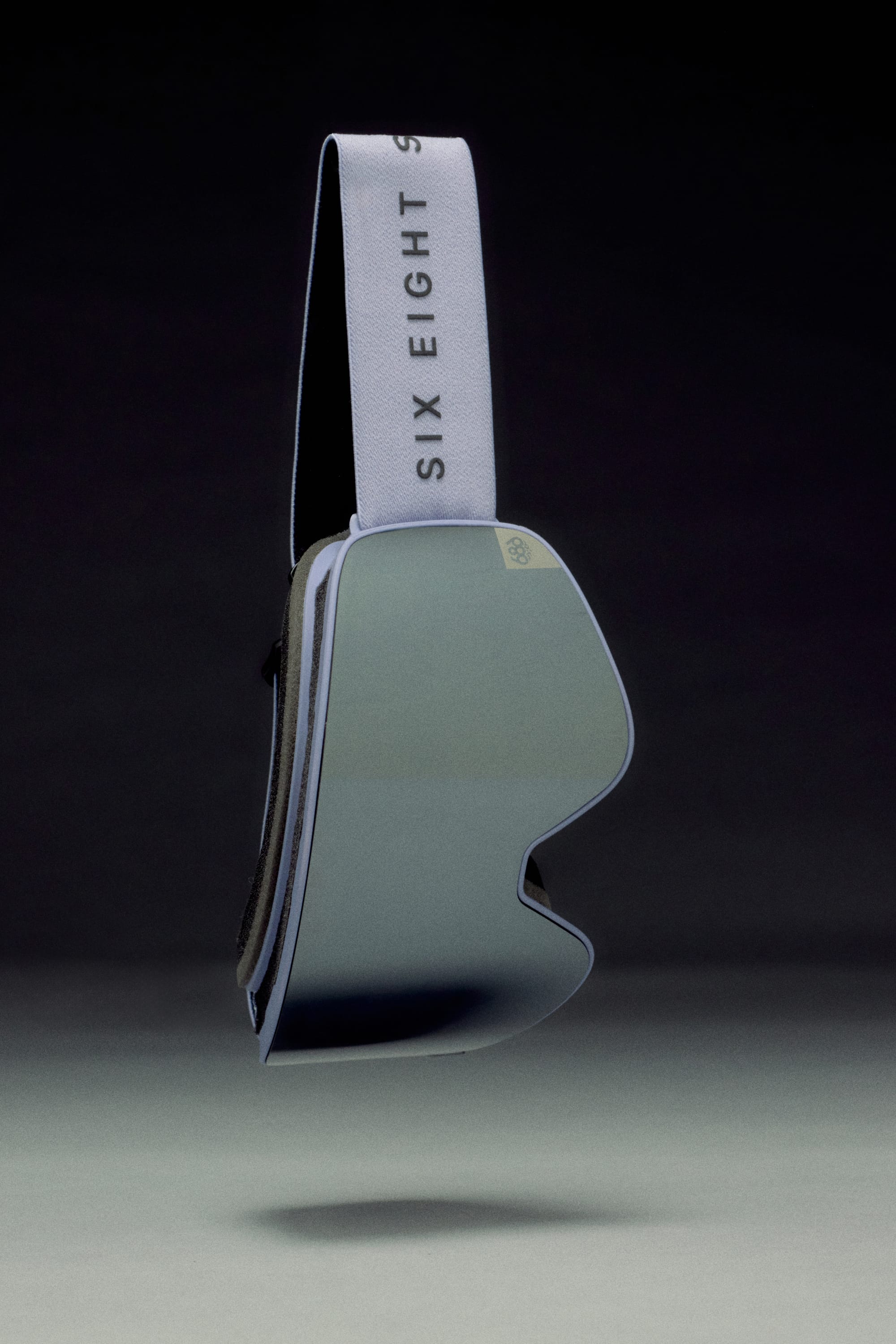 The 686 SMARTY Goggle by 686 features sleek, reflective minimalist magnetic lenses and a white SIX EIGHT strap, showcased against a dark gradient background.