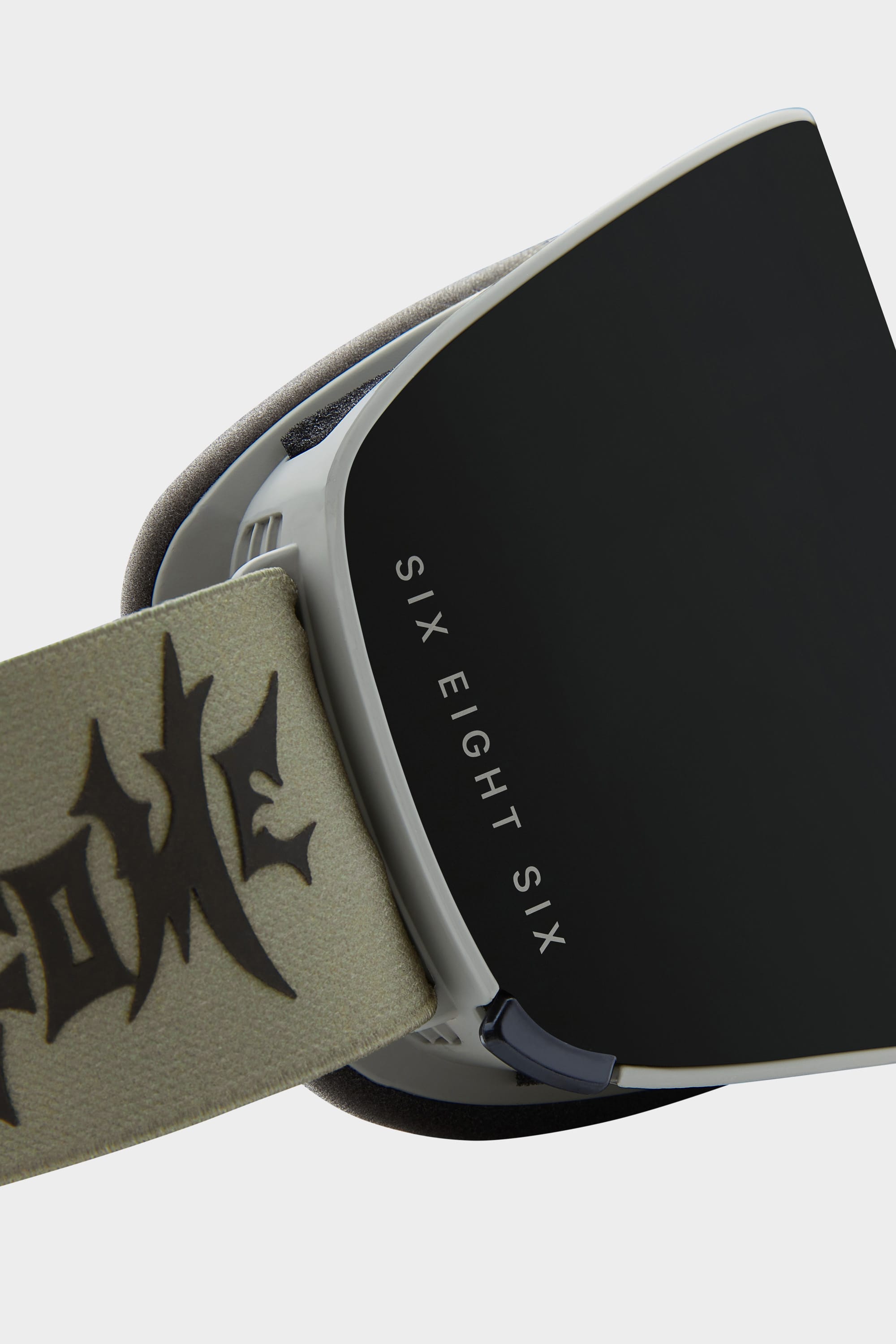 Close-up of the 686 SMARTY Goggle by 686, showcasing a black lens with SIX EIGHT SIX text and a tan strap featuring a graffiti-inspired design. Magnetic lenses make swapping for any conditions quick and easy.