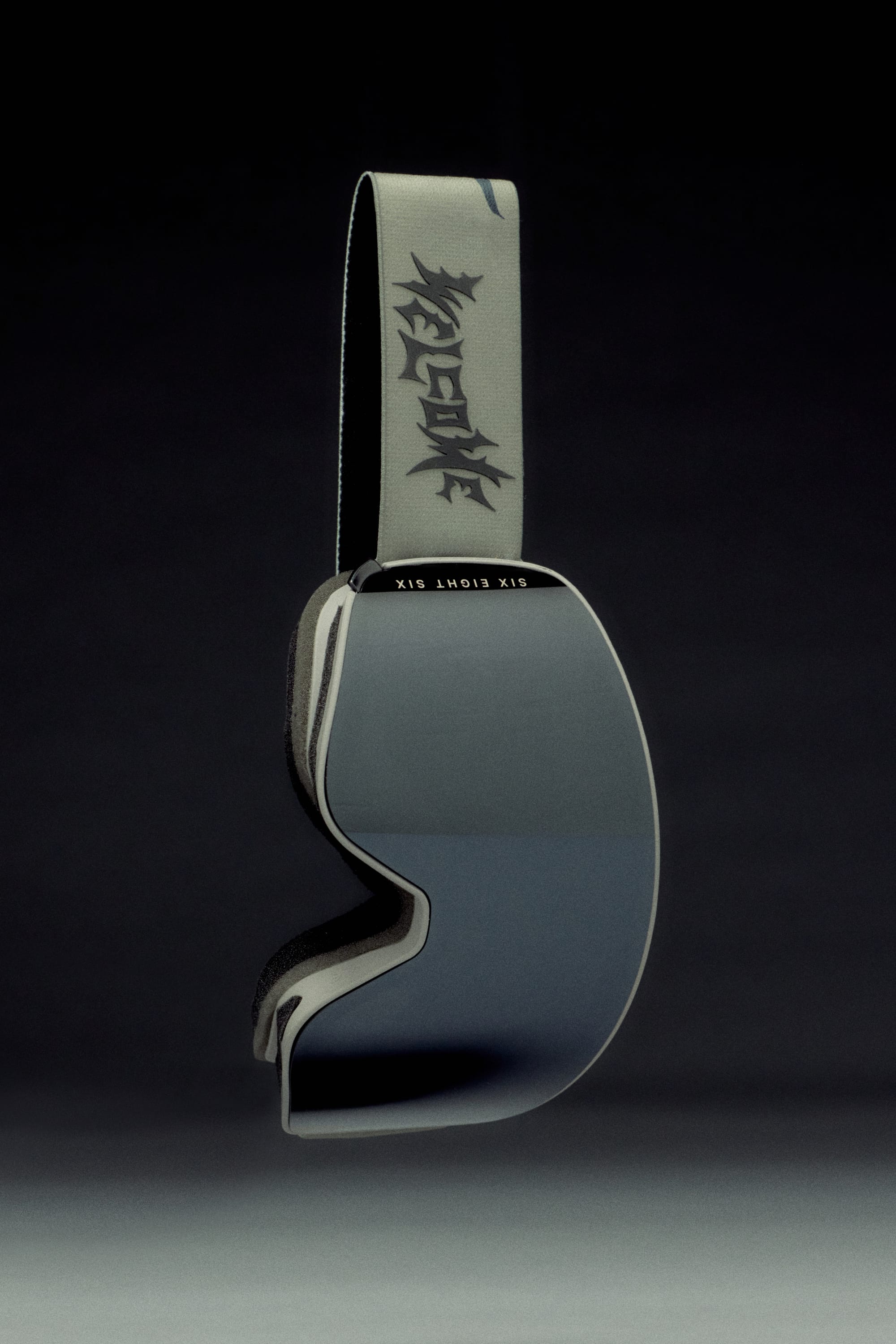 The 686 SMARTY Goggle by 686 features a wide, reflective magnetic lens and a light gray strap with bold black text, offering sleek minimalist style and top performance in all conditions against a dark backdrop.
