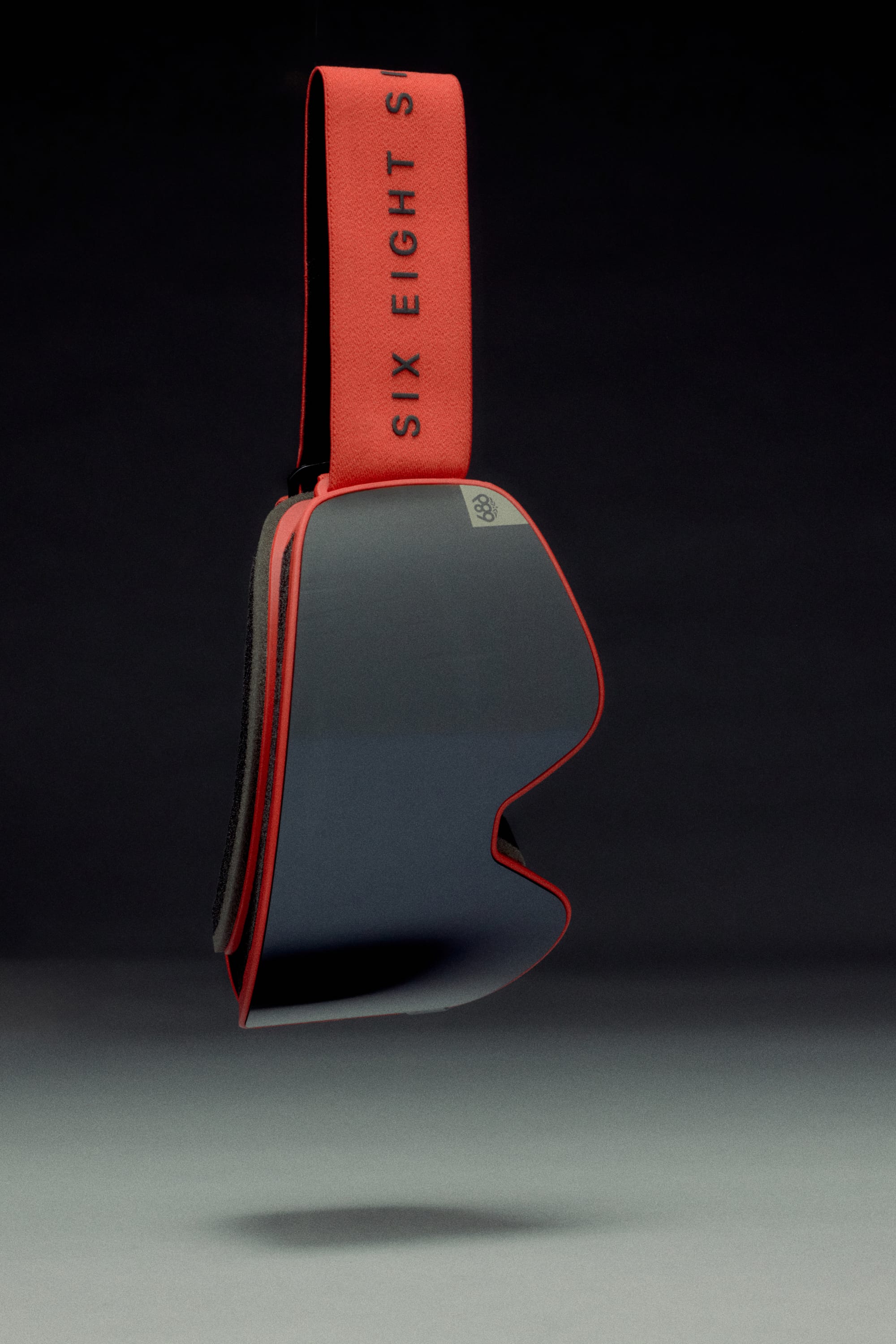 The 686 SMARTY Goggle by 686 features a minimalist design with a reflective lens, red trim, and a red strap emblazoned with SIX EIGHT in black text, suited for all conditions and displayed against a dark gradient backdrop.