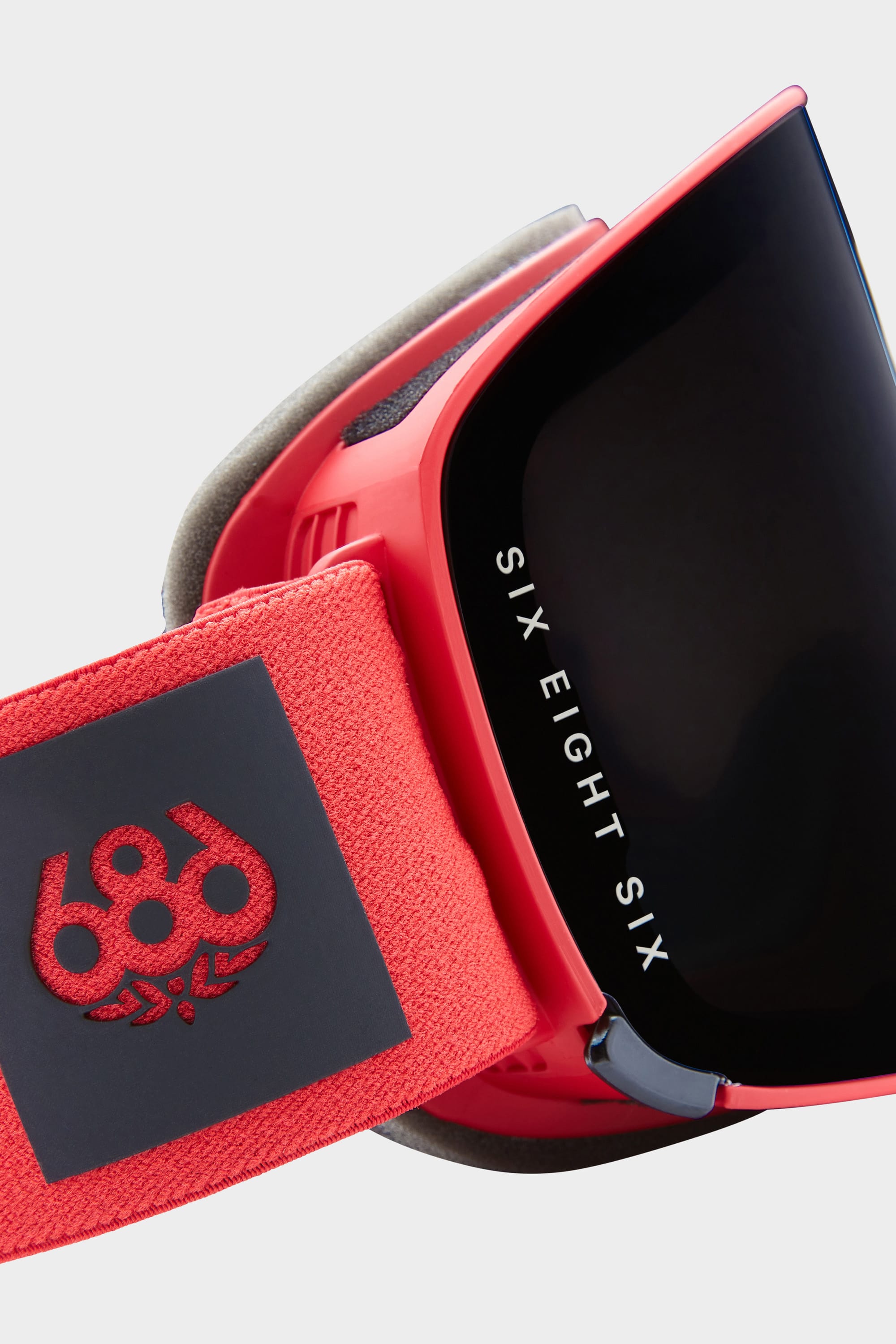 Close-up of the 686 SMARTY Goggle, featuring a red minimalist design, black magnetic lens with SIX EIGHT SIX branding, and a strap embroidered with the 686 logo plus decorative detailing for all conditions.