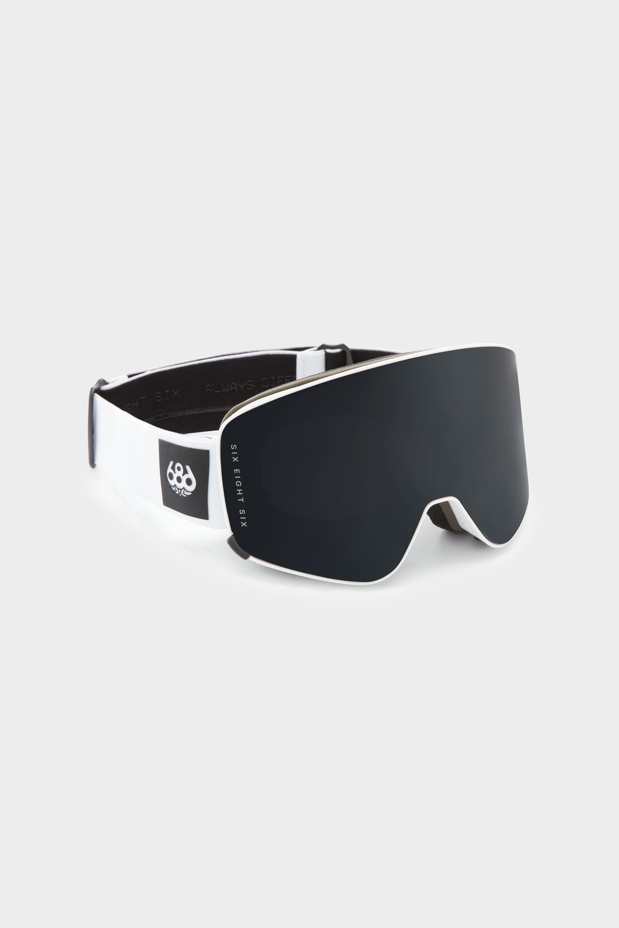 The 686 SMARTY Goggle by 686 features a black and white minimalist design, a reflective dark magnetic lens for easy swaps in any condition, a thick white strap with the 686 logo, and is pictured on a plain light gray background.