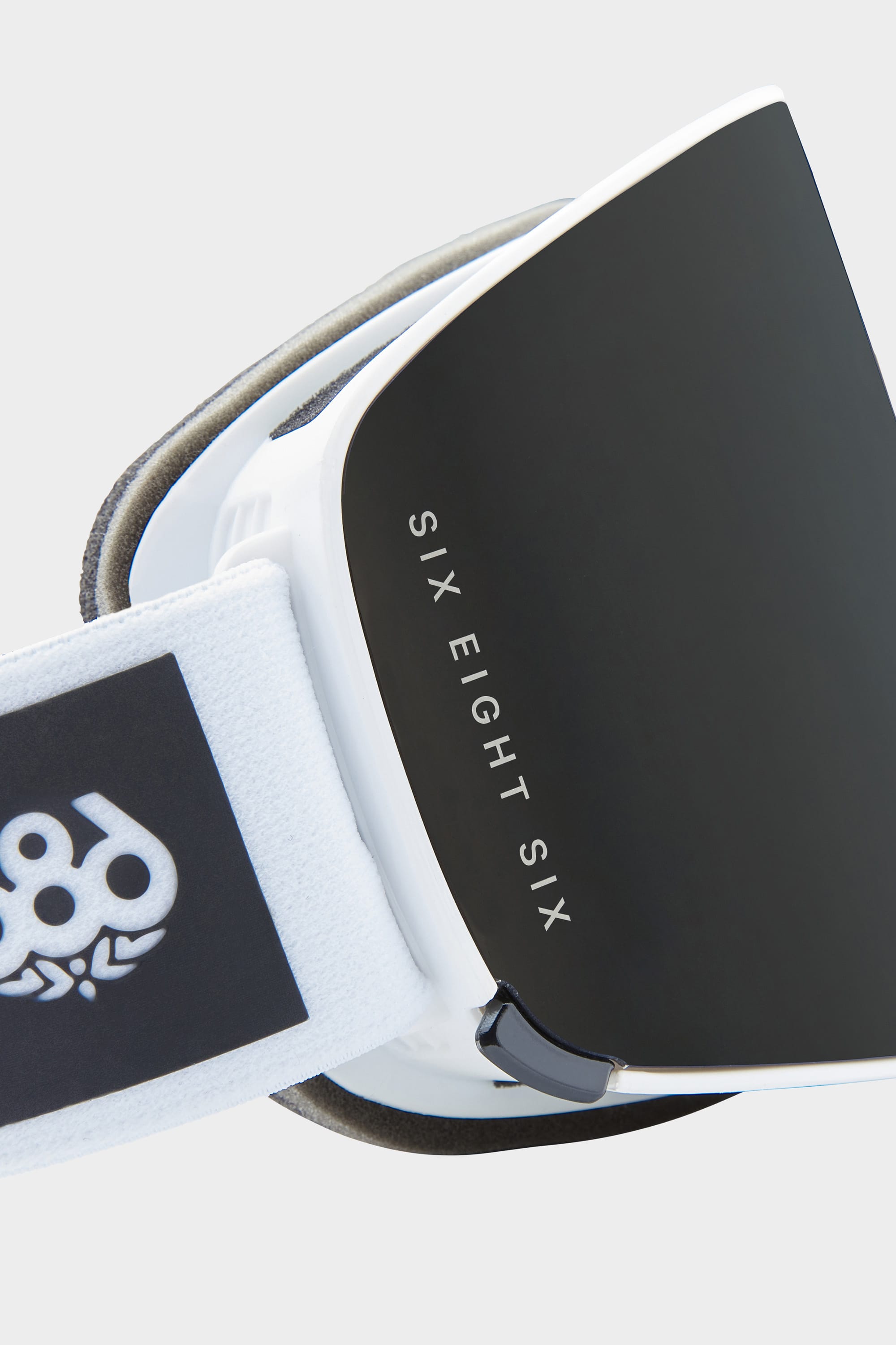 Close-up of the 686 SMARTY Goggle: a minimalist design with black lenses, white frame, and a strap featuring the 686 logo. SIX EIGHT SIX branding appears on the side, while magnetic lenses allow for quick swaps in any condition.