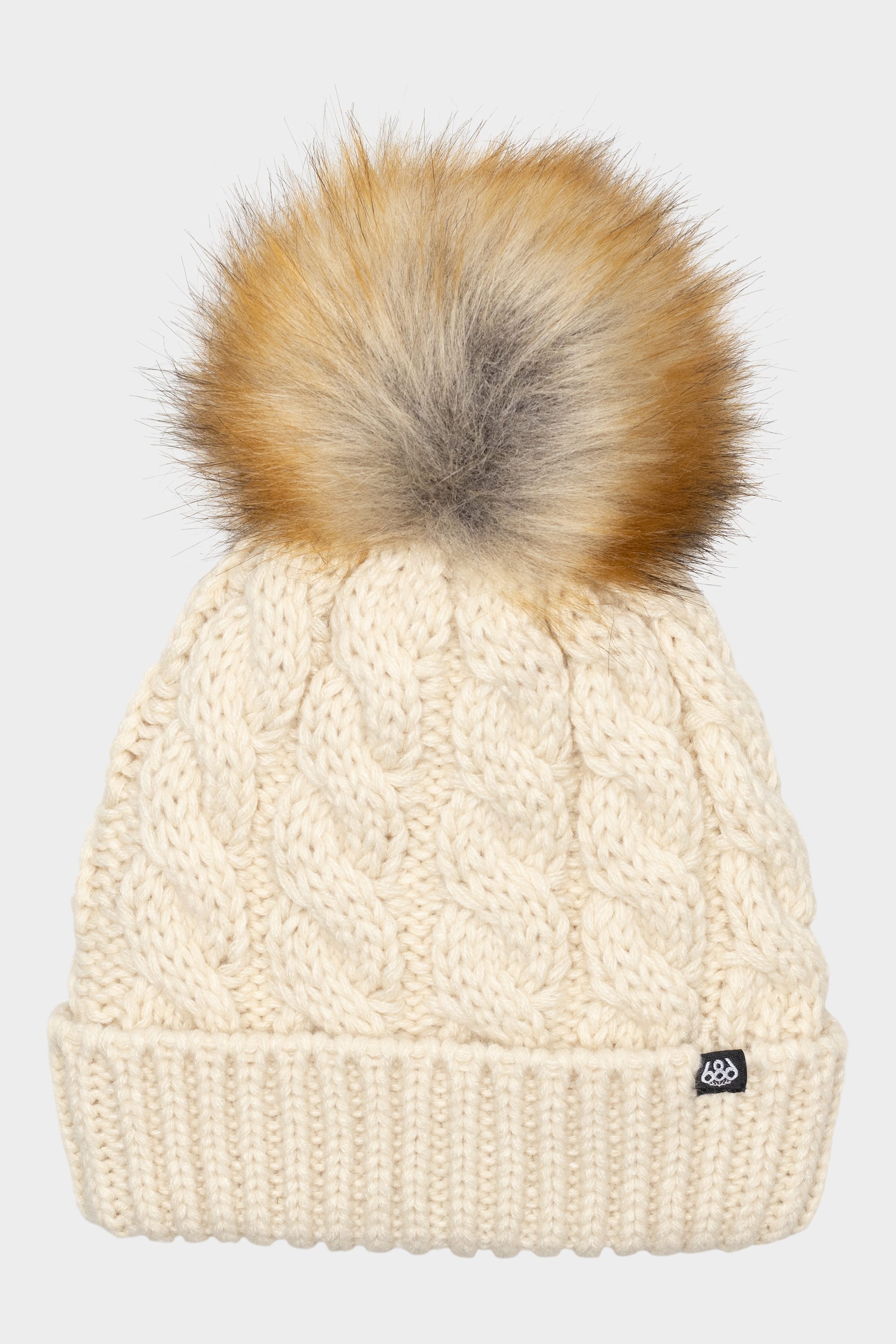 The 686 Girls Knit Pom Beanie by 686 is a cream-colored cable-knit hat featuring a large faux fur pom-pom on top and a small black logo tag on the cuff.