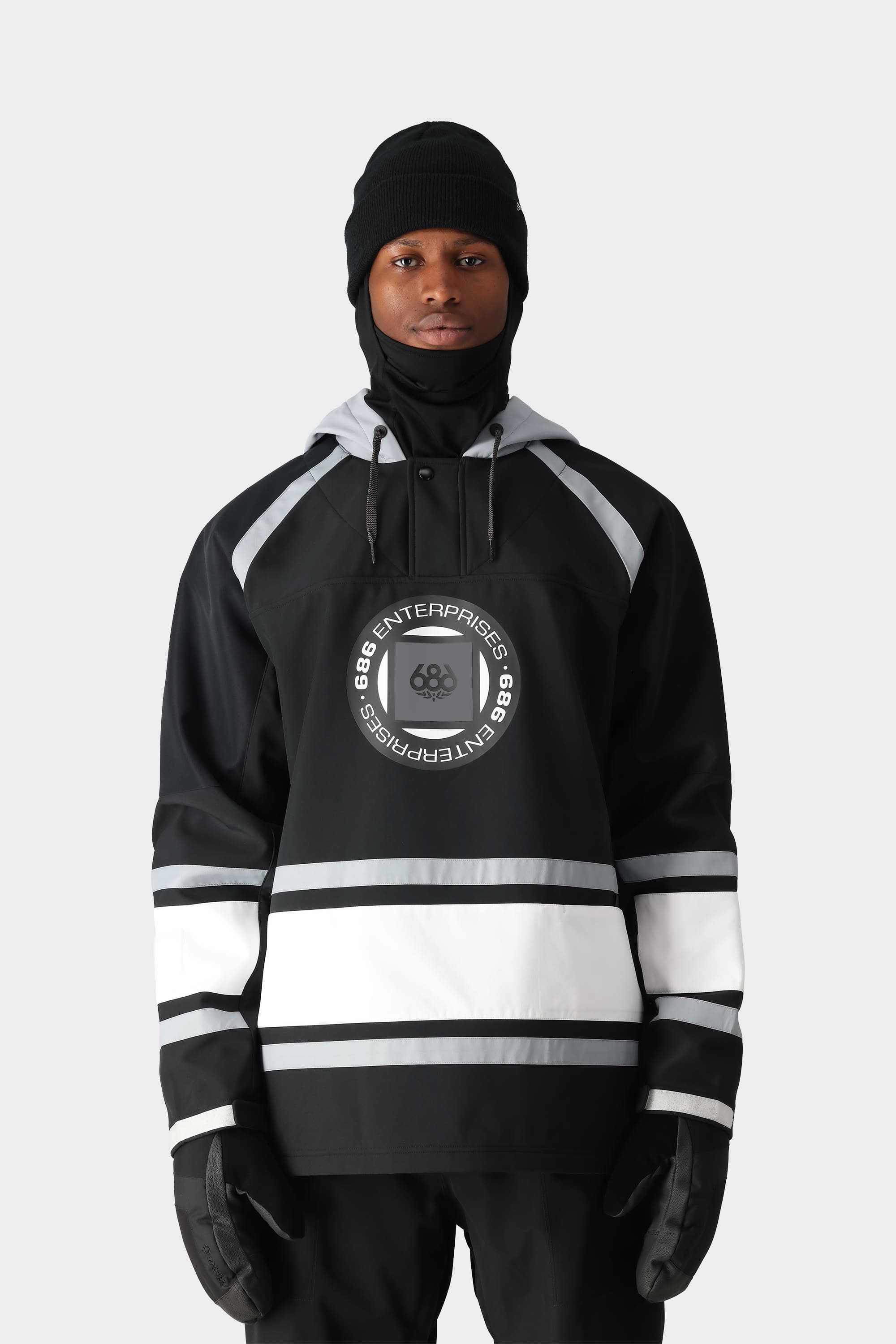 A person wearing the 686 Mens Waterproof Slapshot Hoody by 686, featuring black and white colors, a circular front logo, and 688 ENTERPRISES text, along with black gloves, a knit beanie, and face covering against a plain light background.