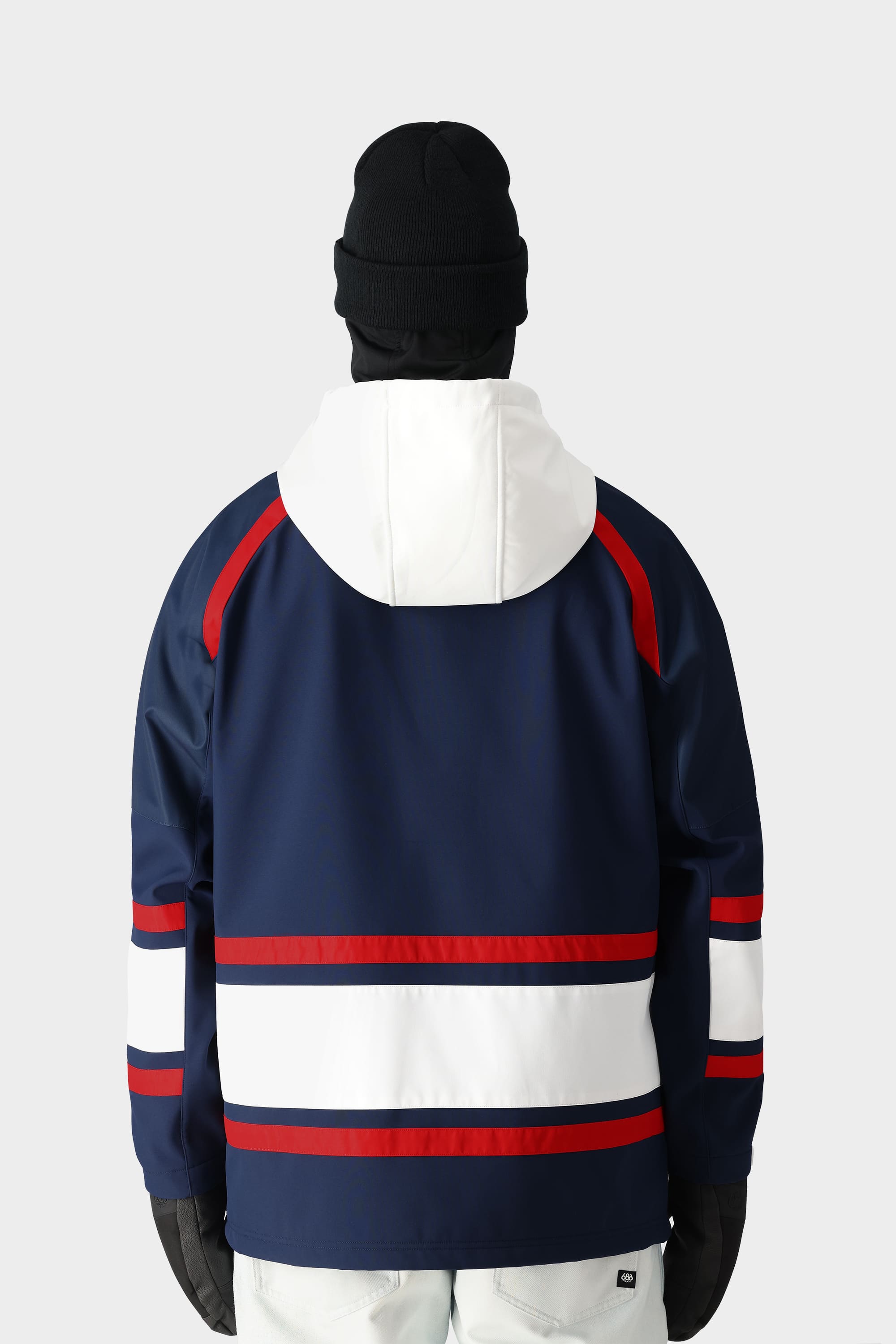 A person in the 686 Mens Waterproof Slapshot Hoody by 686, featuring navy blue with white and red stripes, a white hood, black gloves, black beanie, and light pants stands facing away on a plain background—ready for any resort adventure.