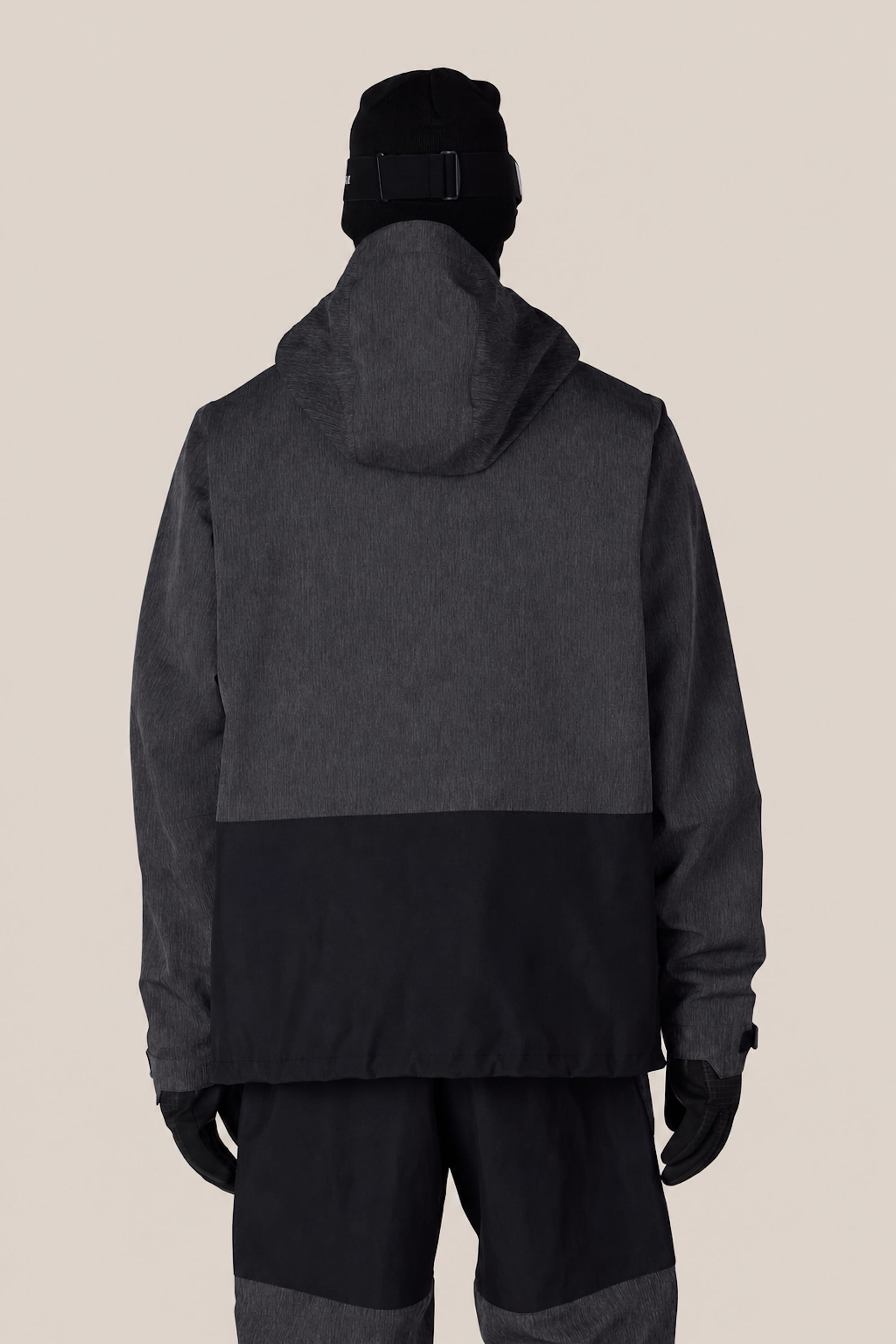 A person wearing the 686 Men’s Ghost™ 2.5L Anorak by 686, along with a black hat and gloves, is shown from the back against a plain beige background.