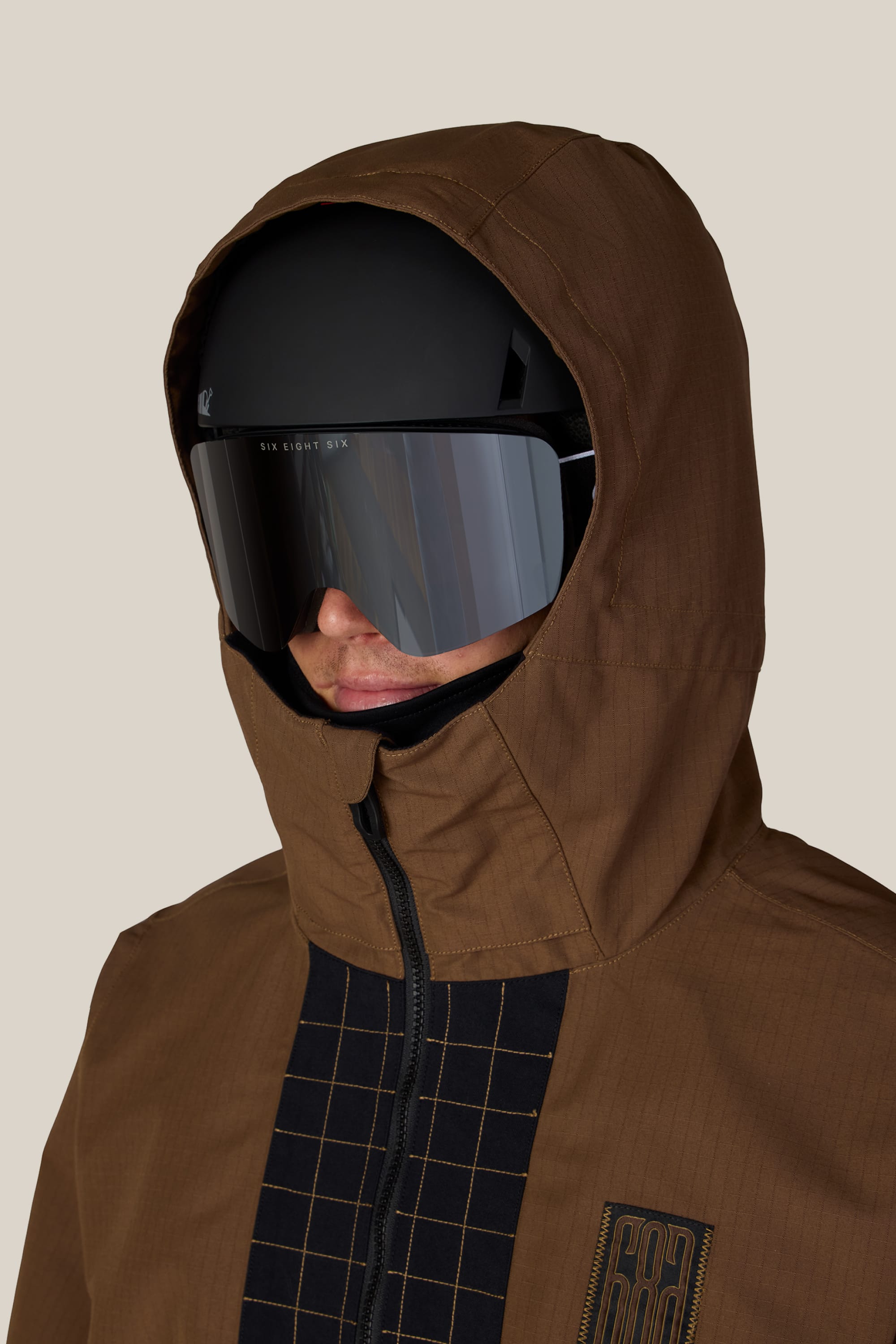 A man wears the 686 Men’s Ghost™ 2.5L Anorak, paired with a black helmet and large reflective ski goggles, facing forward against a plain beige background.