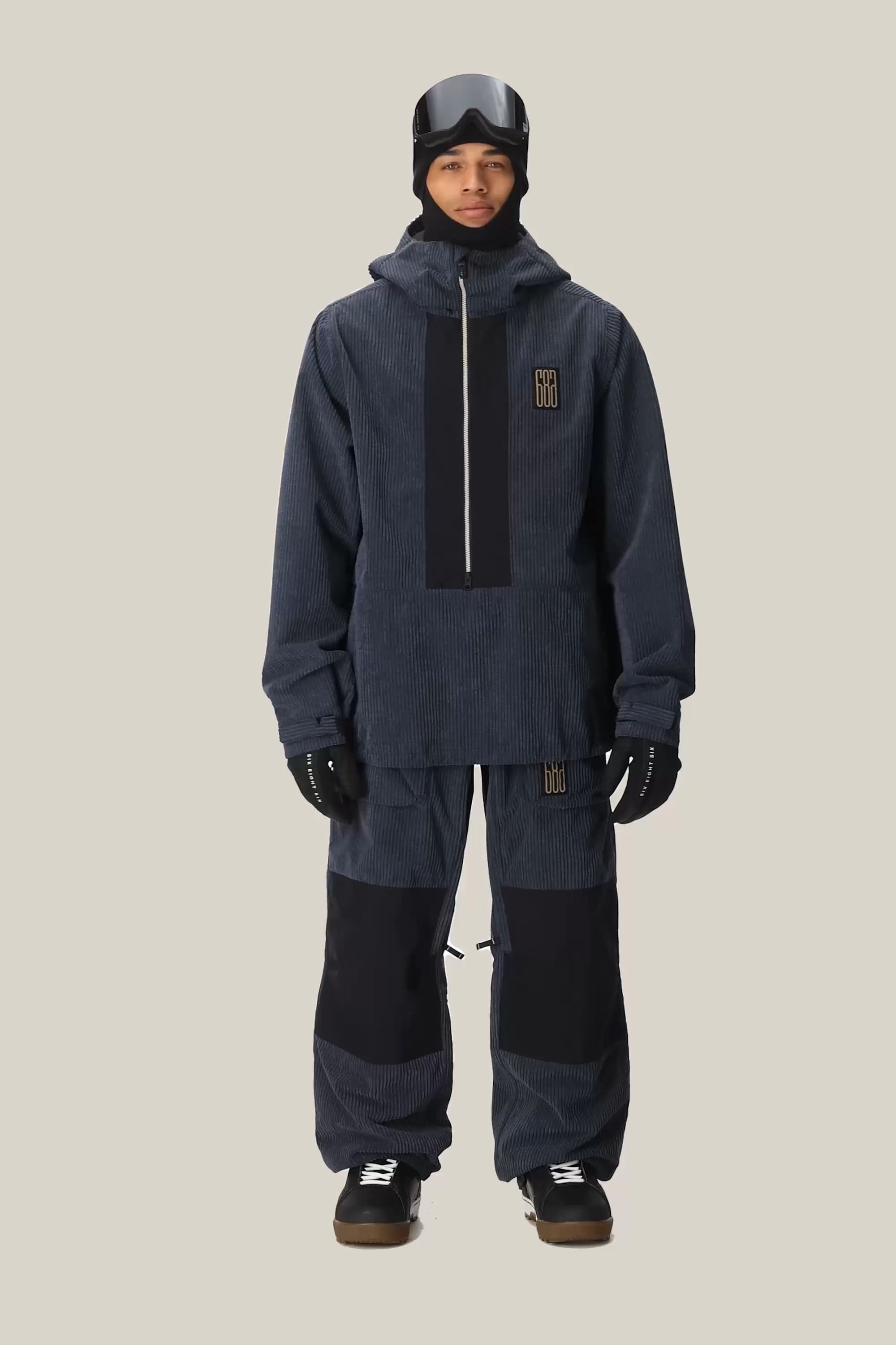 A person wearing the 686 Men’s Ghost™ 2.5L Anorak by 686, paired with matching pants, black gloves, and black snowboard boots, stands facing forward against a plain light background.