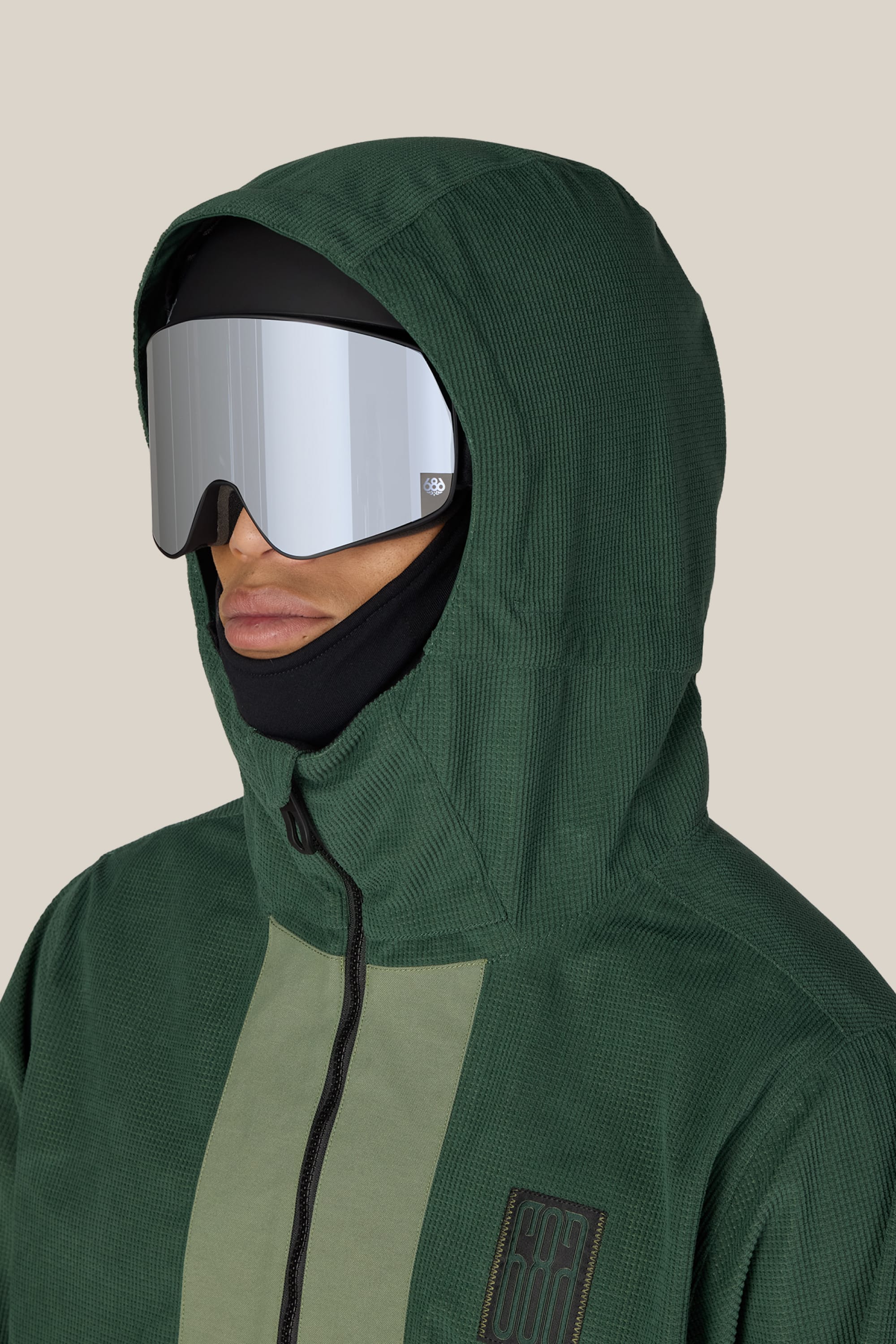 A person wearing the 686 Men’s Ghost™ 2.5L Anorak by 686, paired with a black balaclava and reflective ski goggles, is shown from the shoulders up against a plain beige background.