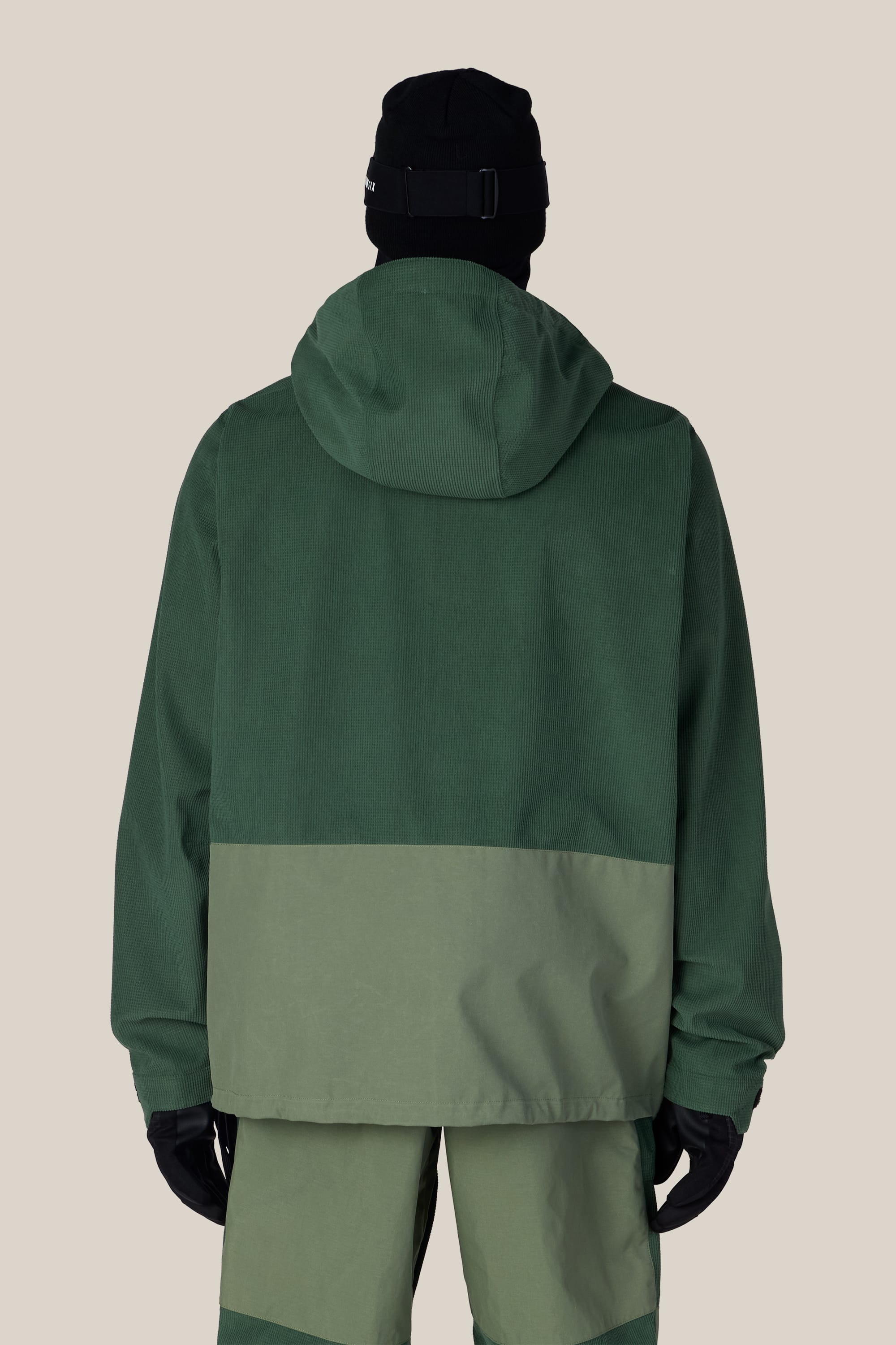 A person is shown from the back against a plain beige background, wearing the 686 Men’s Ghost™ 2.5L Anorak by 686 in two-tone green, paired with matching pants, black gloves, and a black beanie.