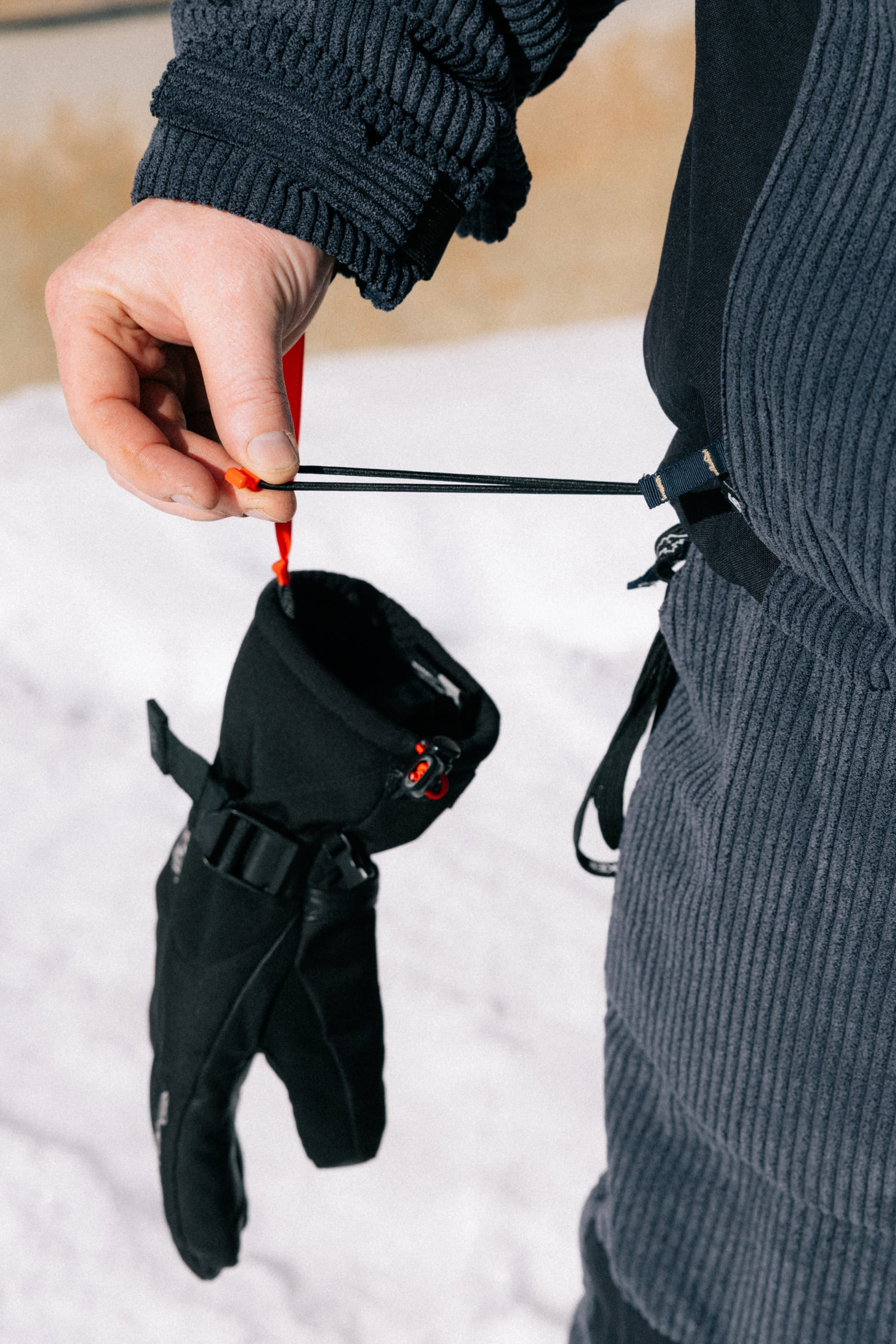 A person wearing the 686 Men’s Ghost™ 2.5L Anorak holds a black glove attached to a clip and elastic cord, with snow visible in the background.