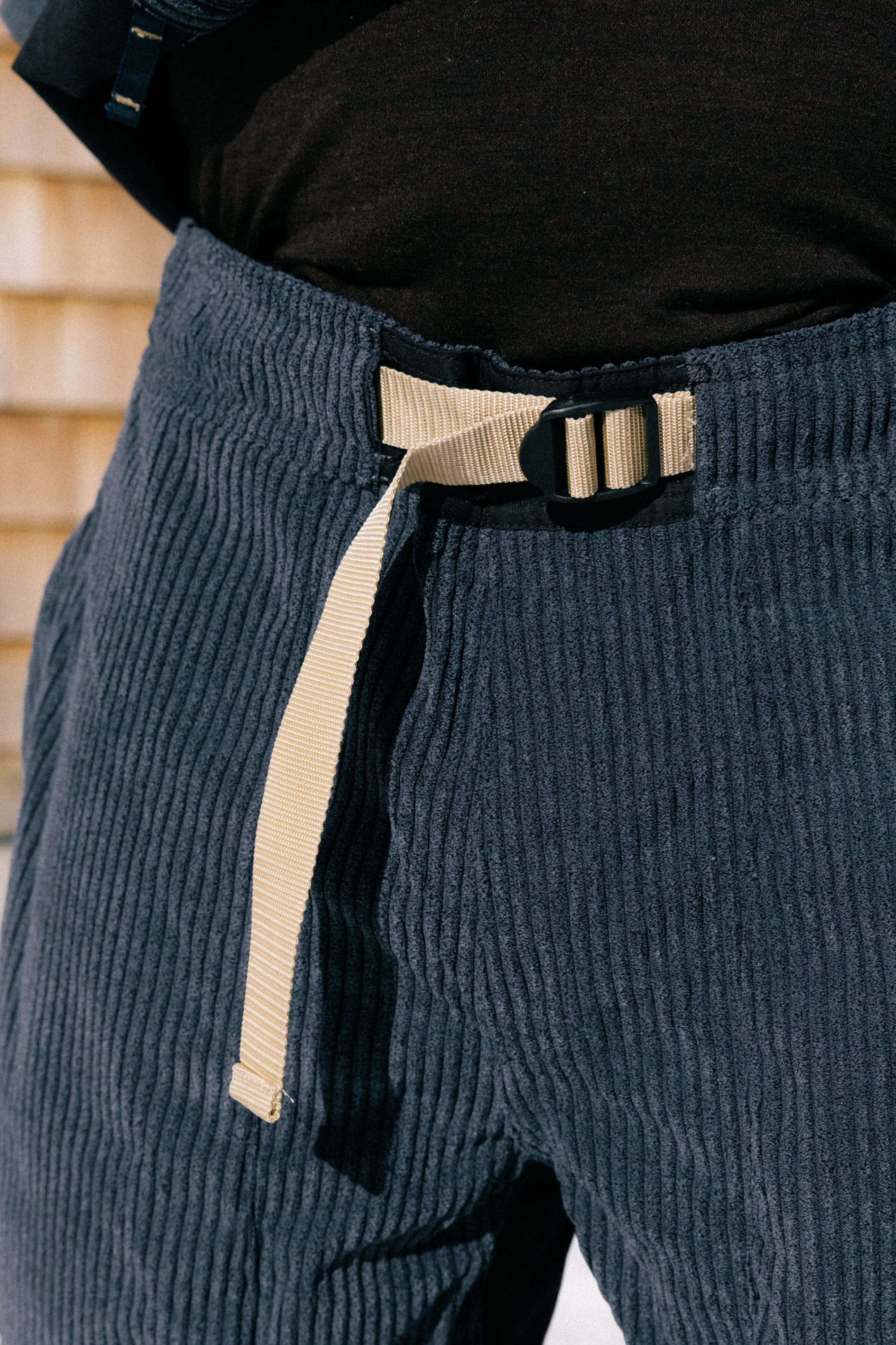 Close-up of a person wearing the 686 Ghost™ 2.5L Pant by 686 in navy blue, styled with a beige fabric belt featuring a black buckle, and paired with a black shirt.