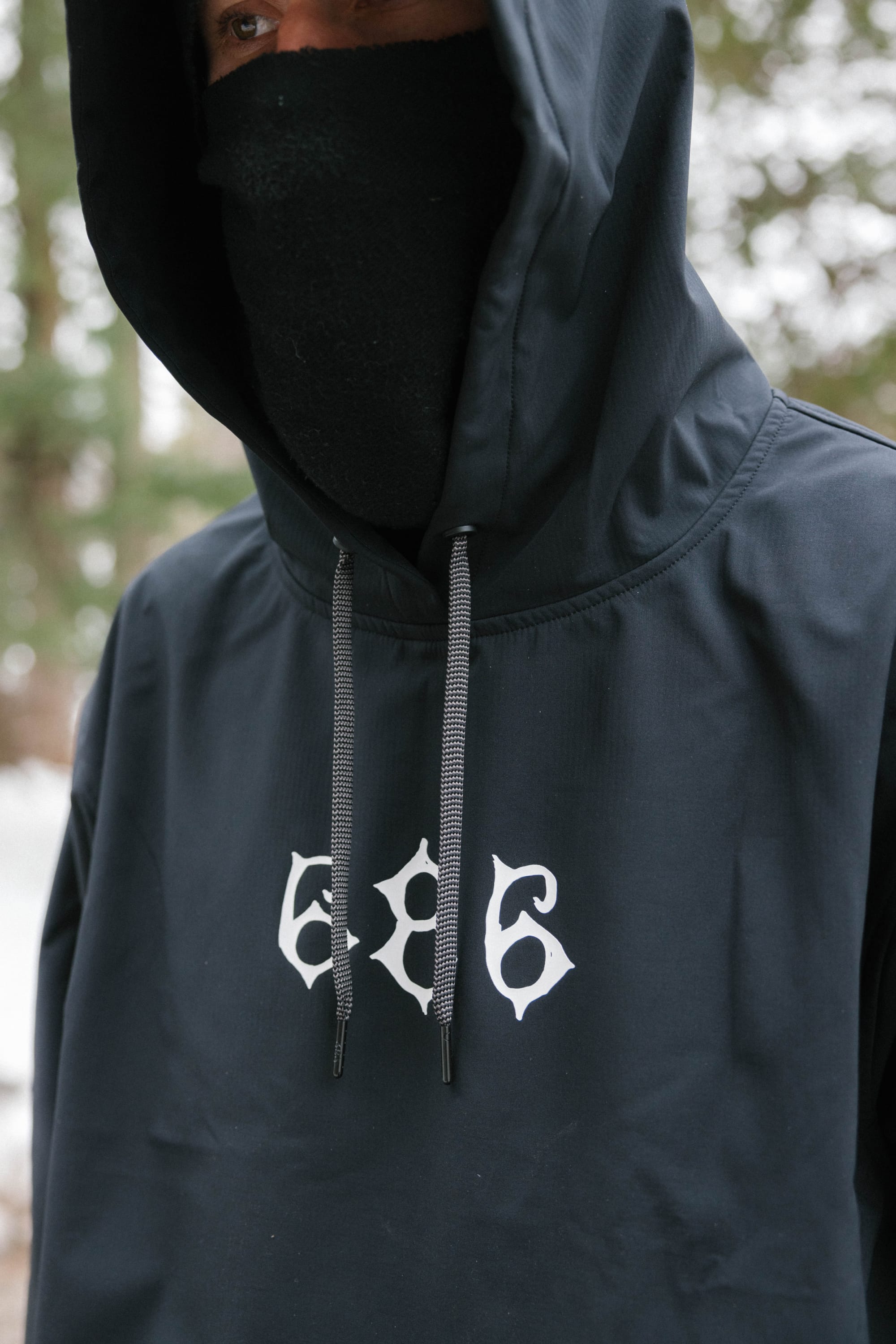 A person in black ski gear poses against a light background, wearing the 686 Mens Waterproof Team Hoody by 686, along with gloves, goggles, and patterned snow pants.