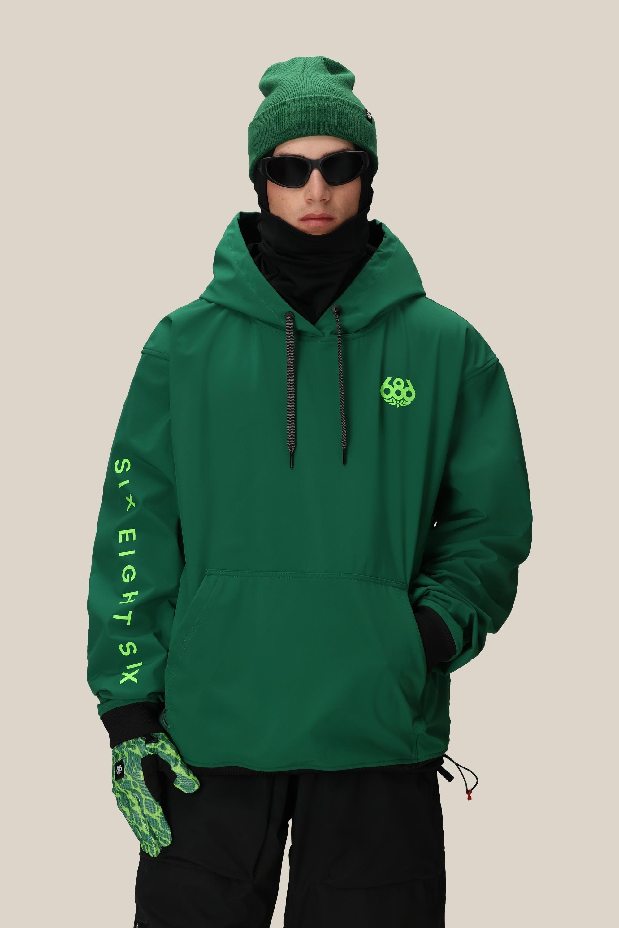 Wearing the 686 Mens Waterproof Team Hoody, a skier soars in midair above a snow ramp, framed by mountain peaks, snowy trees, and a partly cloudy sky.