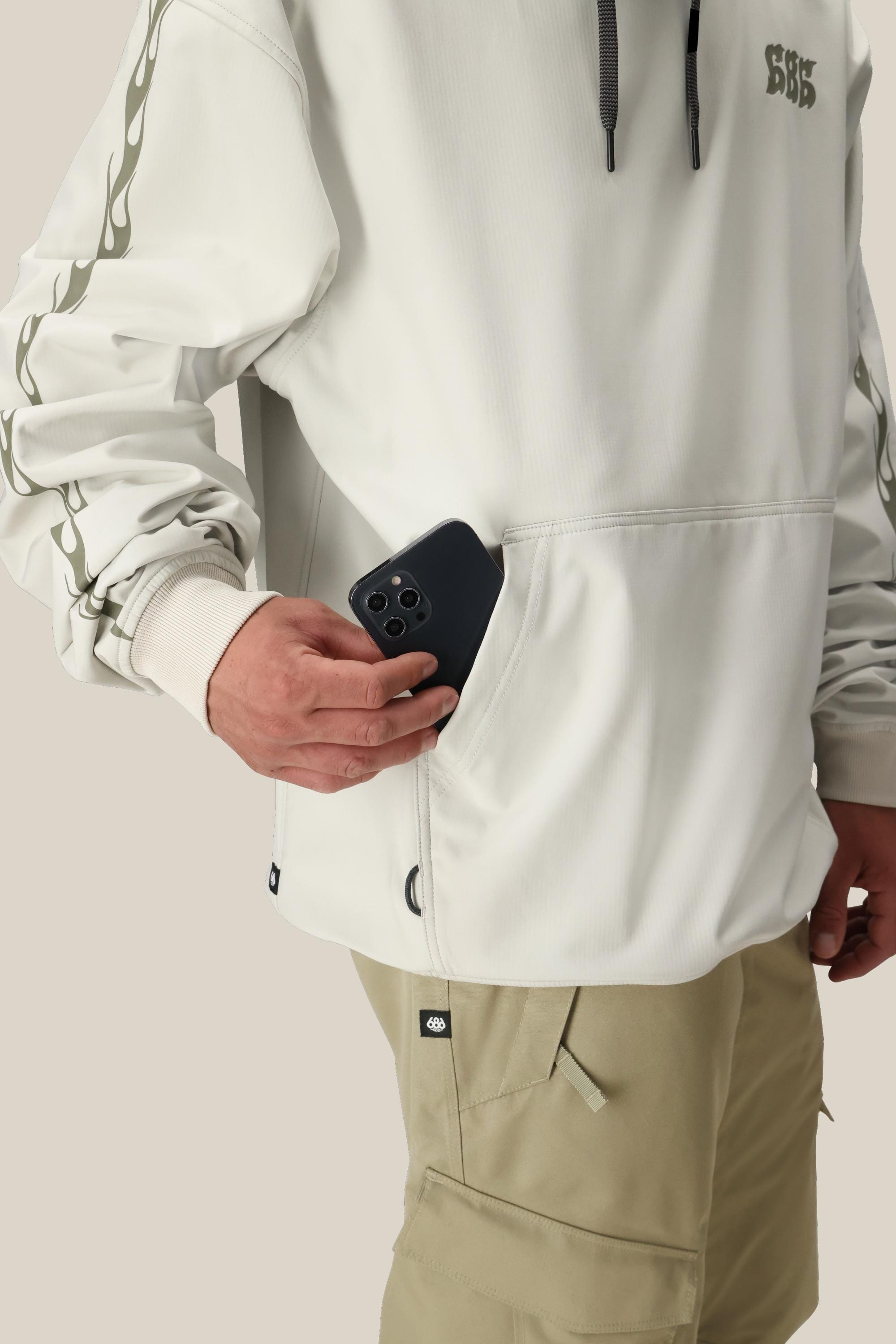 A person in a light purple 686 Mens Waterproof Team Hoody, black ski goggles, balaclava, and gloves stands against a white background.