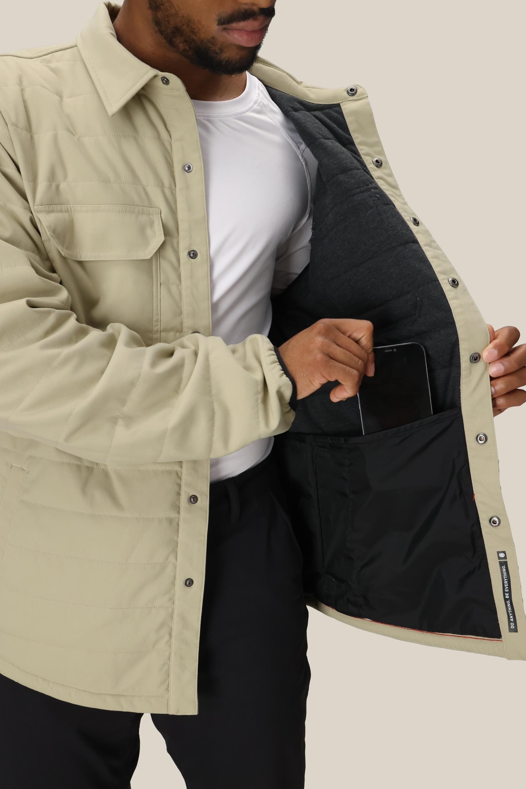 A man in the 686 Mens Thermaldry Snap-Up Shirt opens his jacket to reveal a large inner pocket, effortlessly combining city style with practical performance—ideal for carrying a tablet on the go.