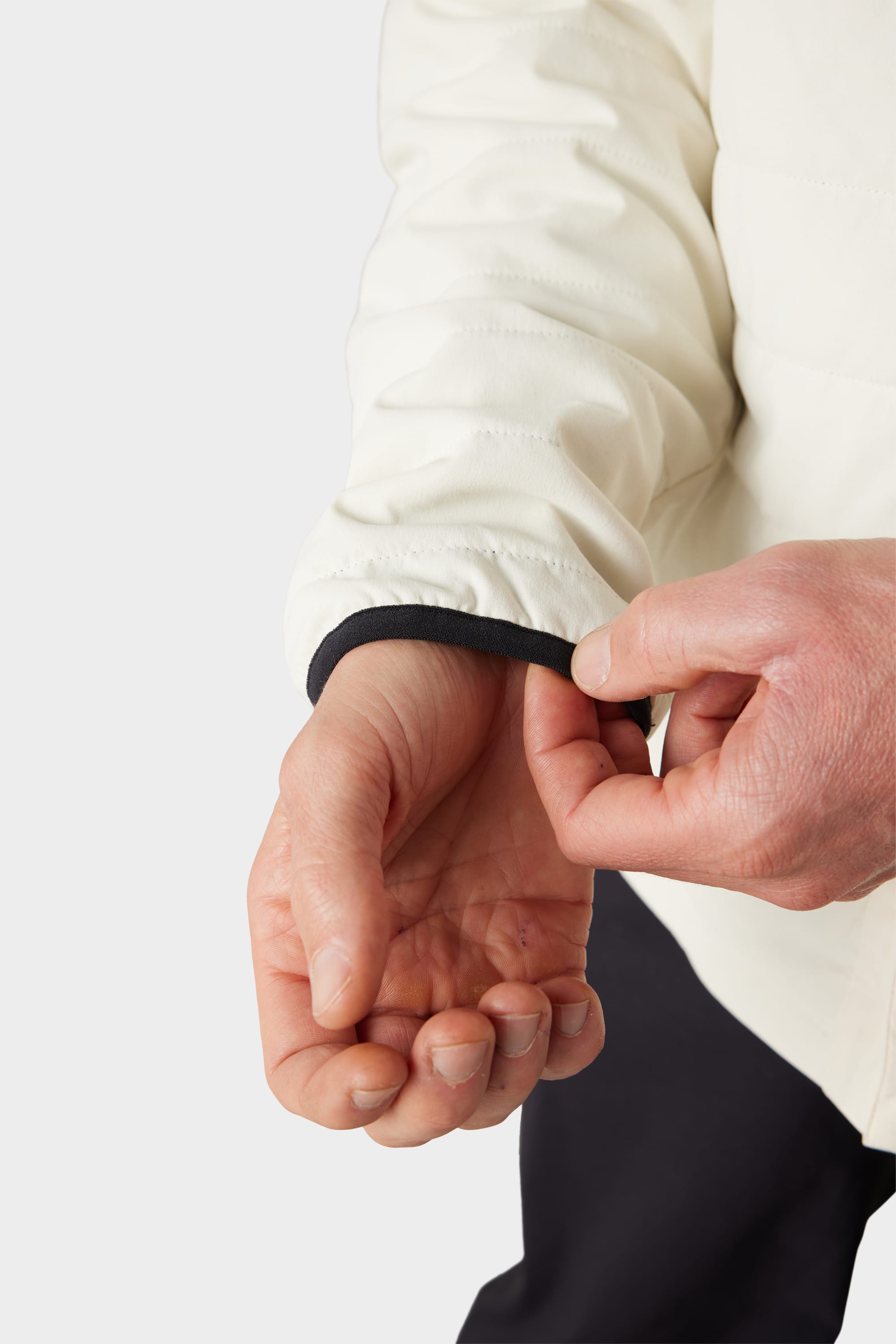 A person uses their right hand to pull the black cuff of the 686 Mens Thermaldry Snap-Up Shirt, a long-sleeve white merino blend by 686, over their left wrist. The background is plain and light-colored.