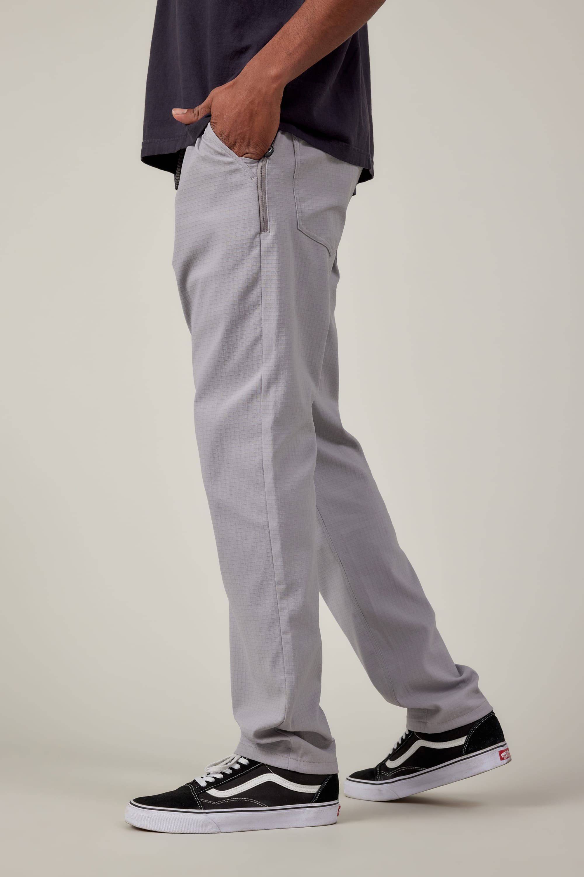 A person is shown from the waist down wearing 686 Mens Everywhere Ripstop Pant - Slim Fit in light grey, paired with a dark short-sleeve shirt and black-and-white Vans sneakers, standing with one hand in their pocket against a light background.